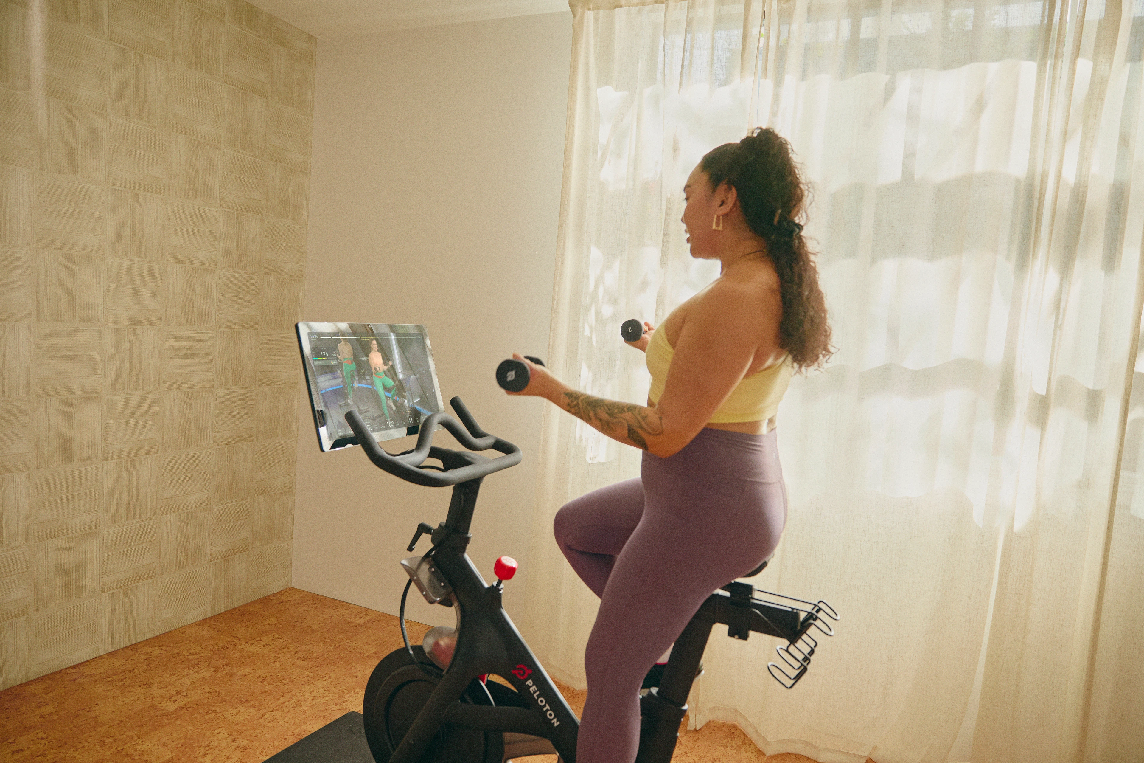 Woman working out on a Peloton Bike doing a light-weight, high-rep arm workout.