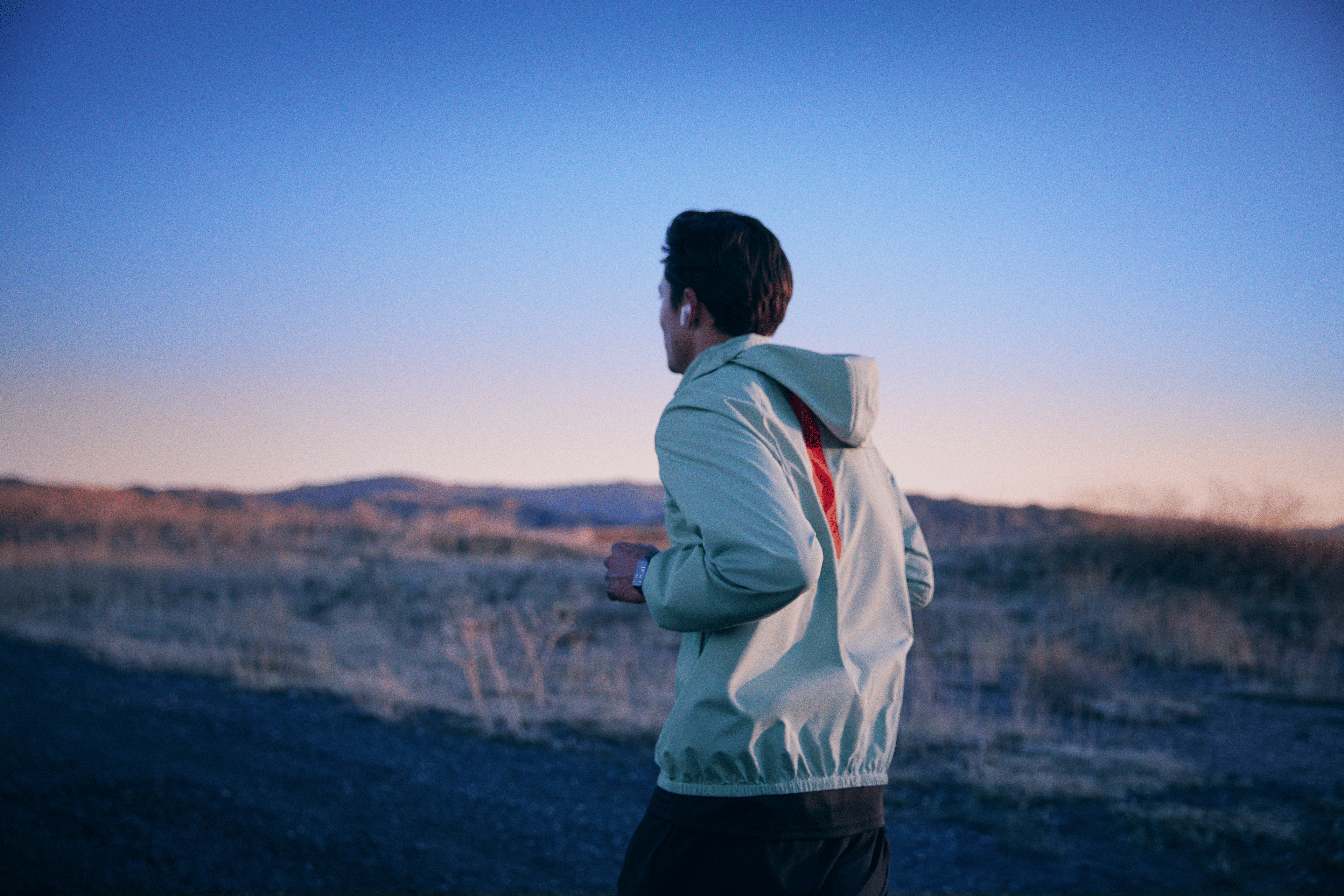 Man on a run outside at twilight while listening to a guided running workout on the Peloton App.