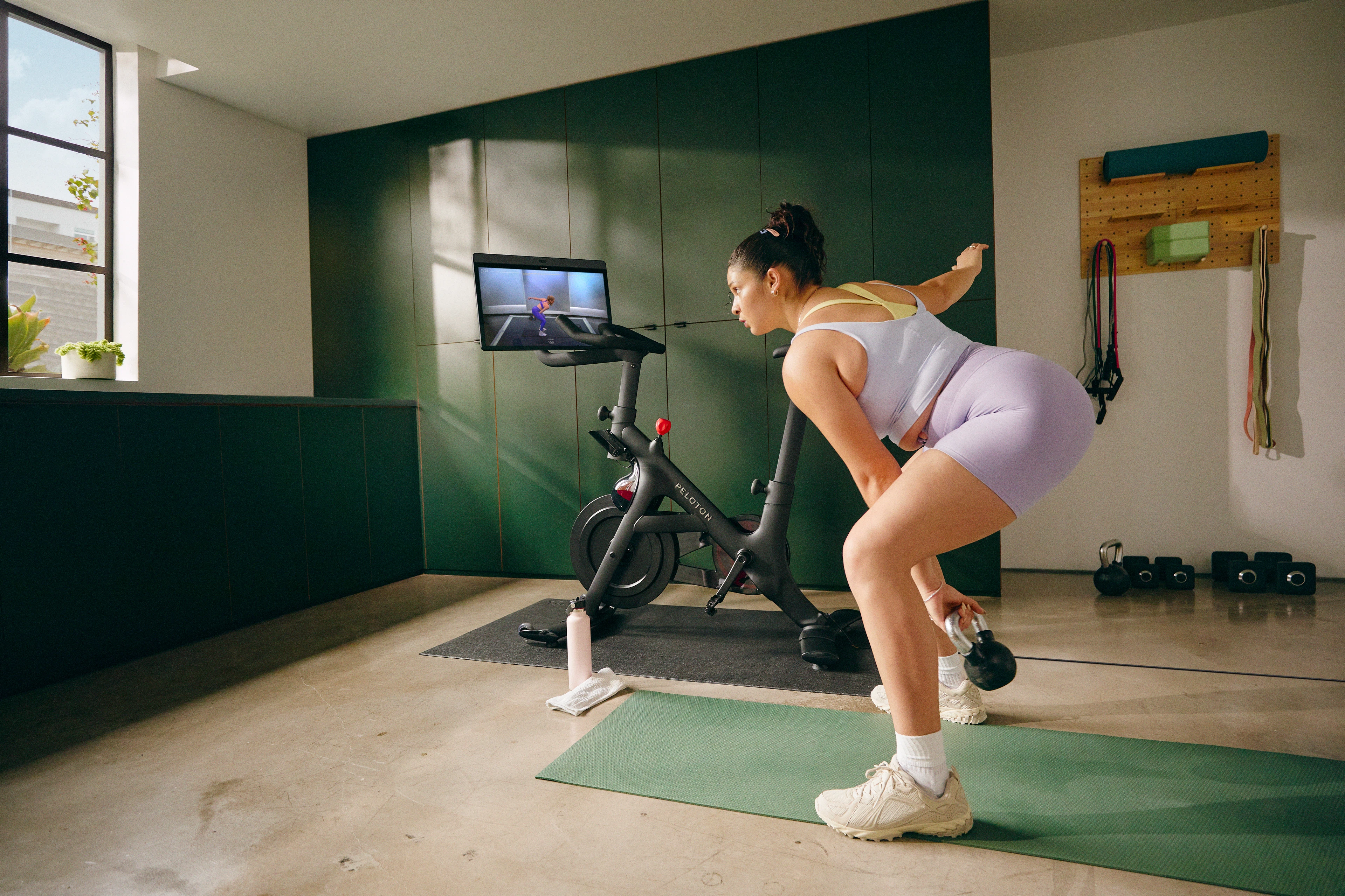 Woman engaging in hybrid training by doing a Peloton kettlebell strength class on her Bike+.