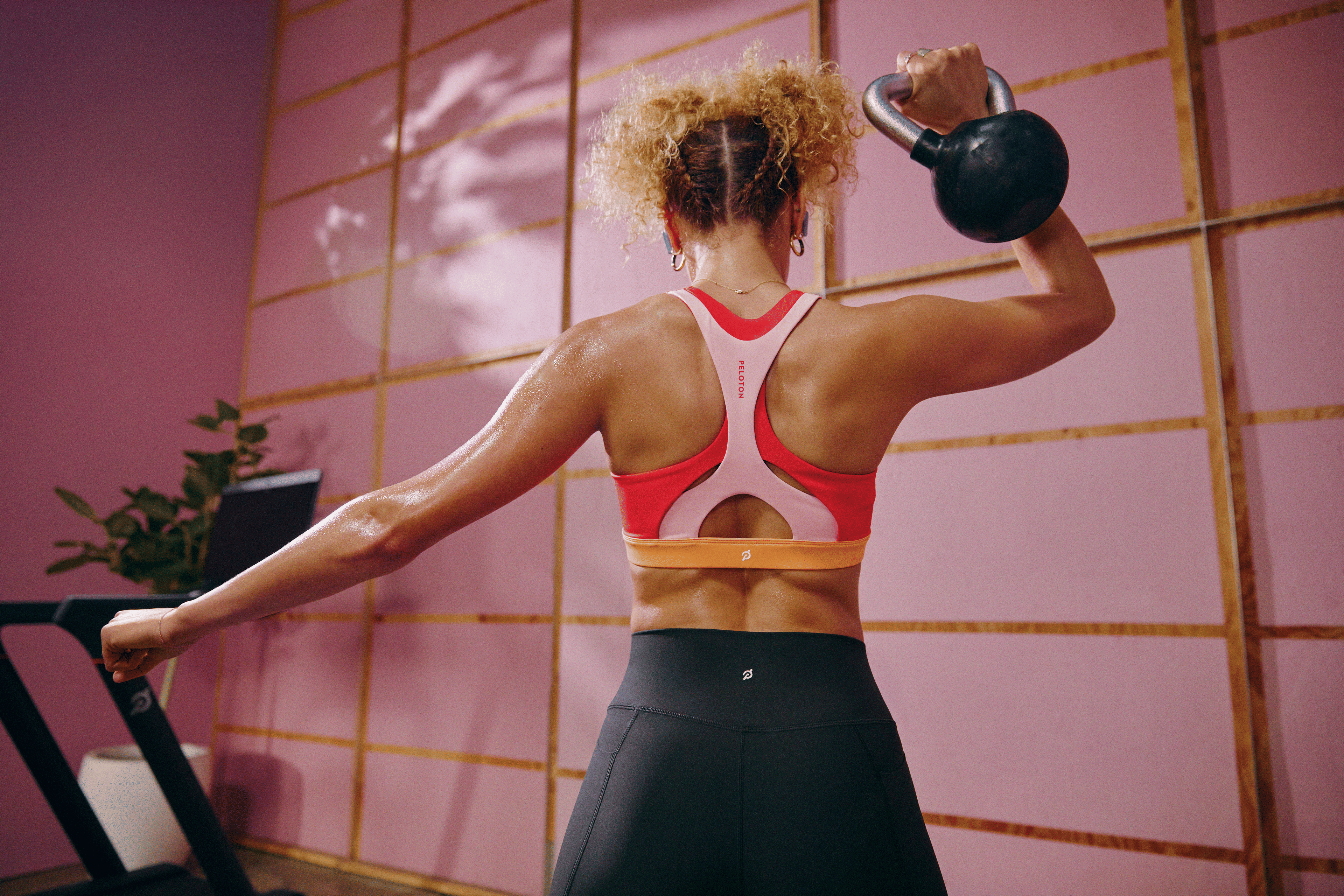 Woman in a sports bra pressing a kettlebell during a Peloton strength training workout.