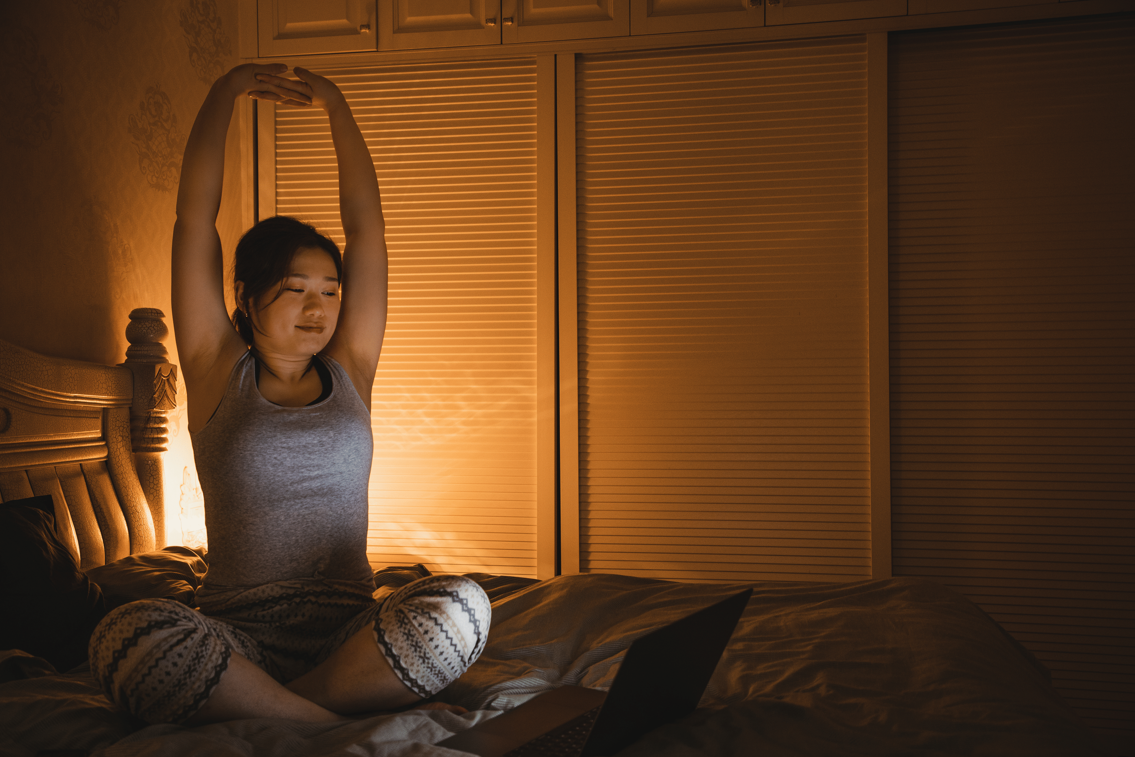 Woman stretches while sitting on bed
