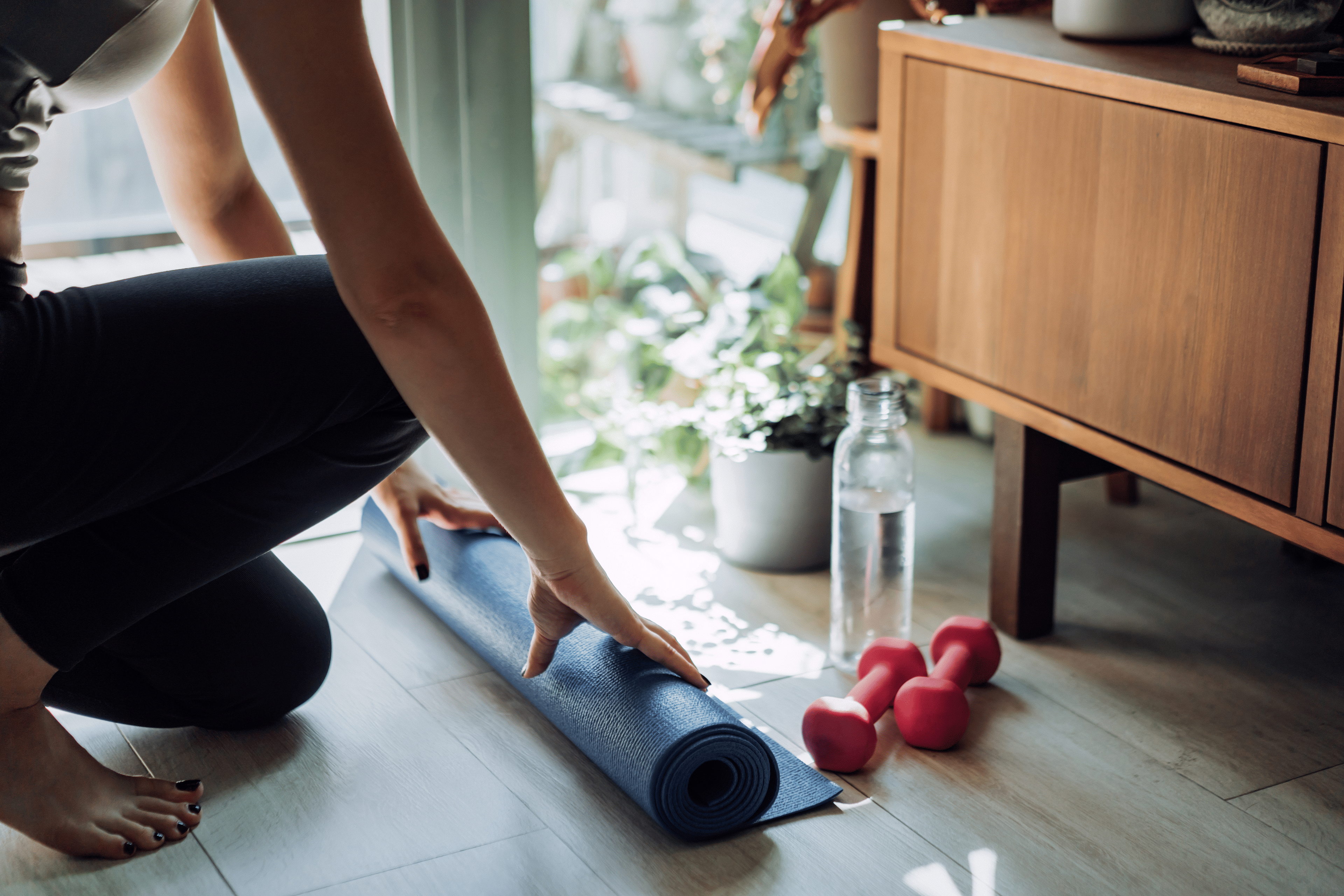 Woman rolling out exercise mat for a home workout deciding whether to do Pilates vs weight training