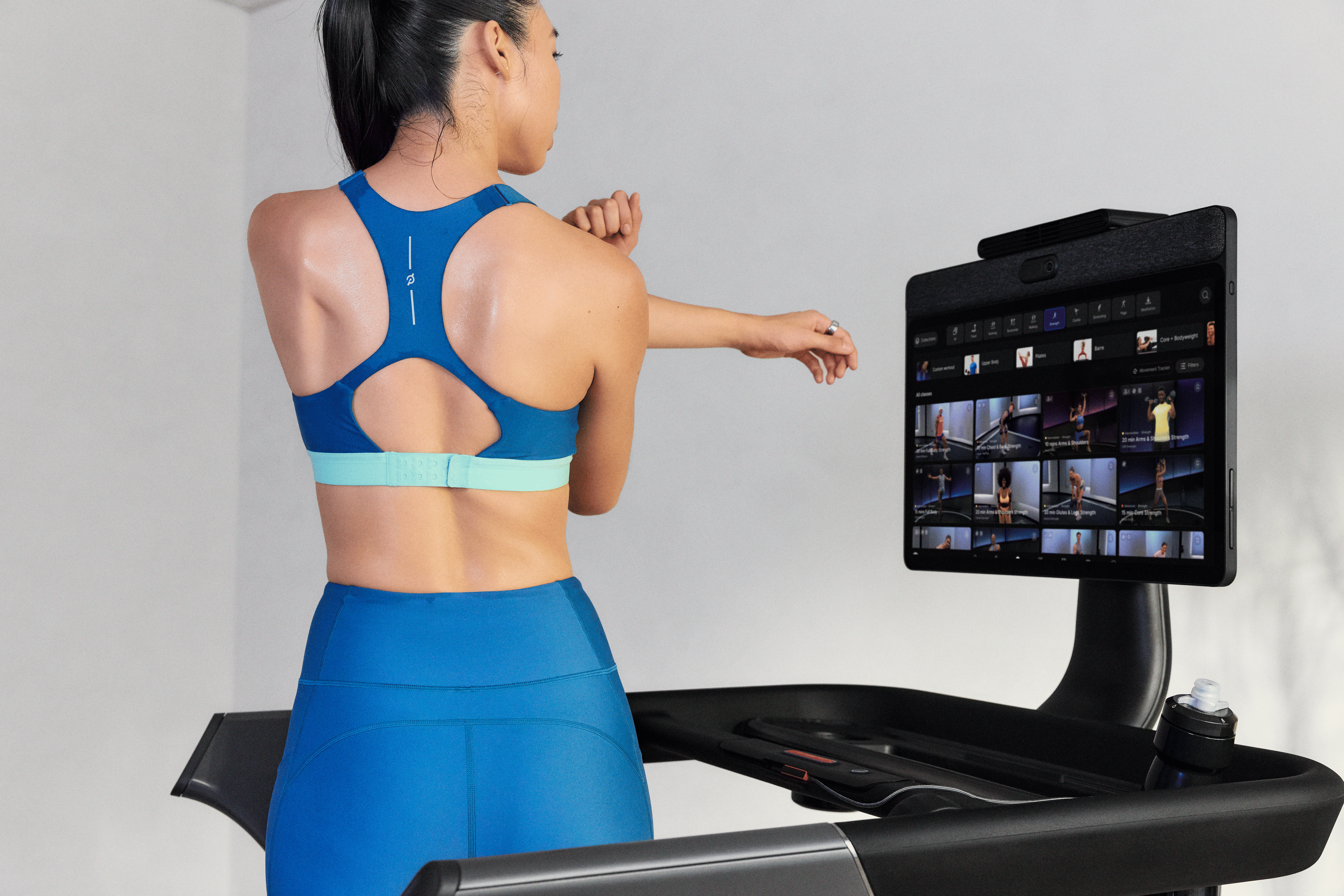 Woman in Peloton Apparel stretching while standing on the Peloton Cross Training Series Tread+