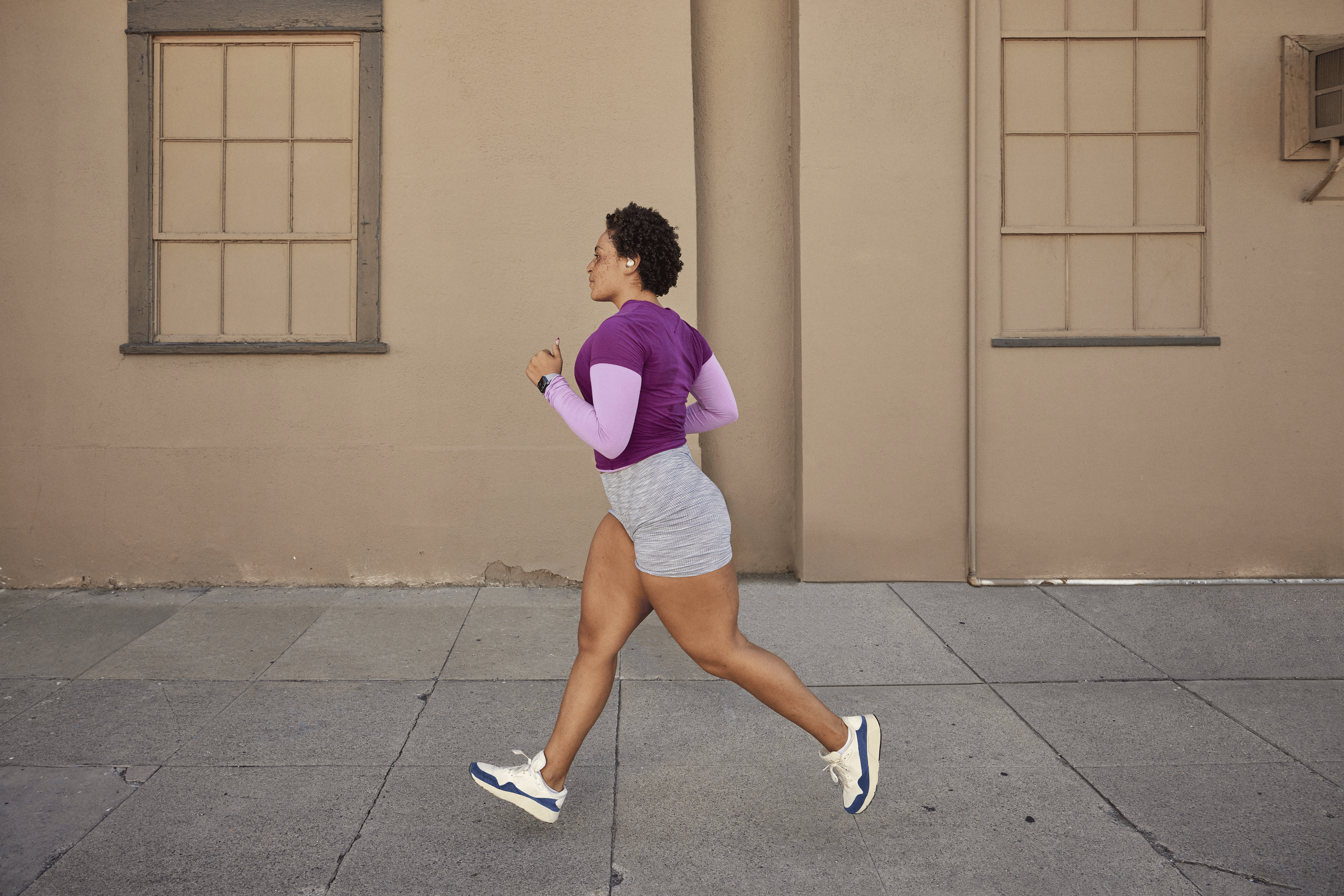 Woman in a purple shirt and grey shorts doing the run-walk method outside past a blank wall