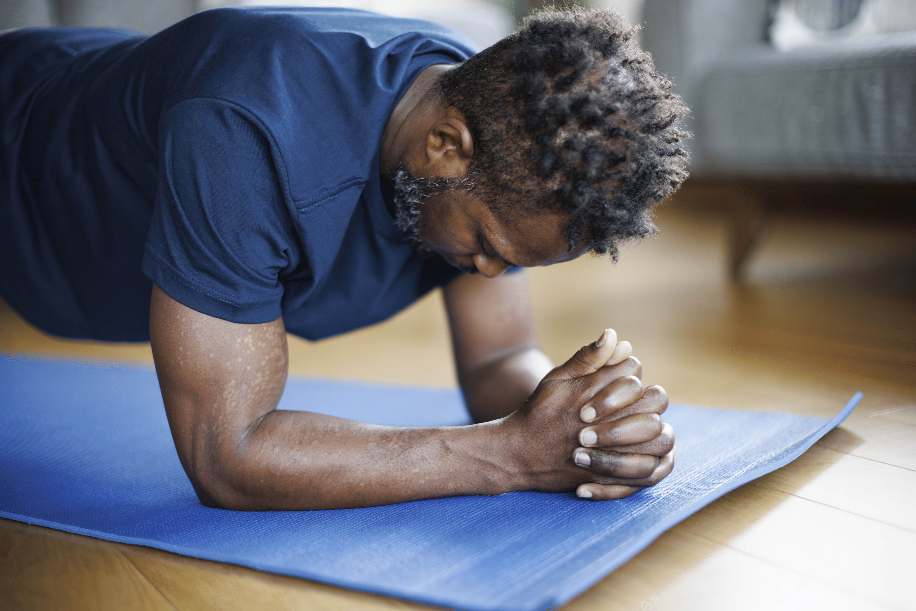 Man in a blue shirt doing a forearm plank during a bodyweight workout at home