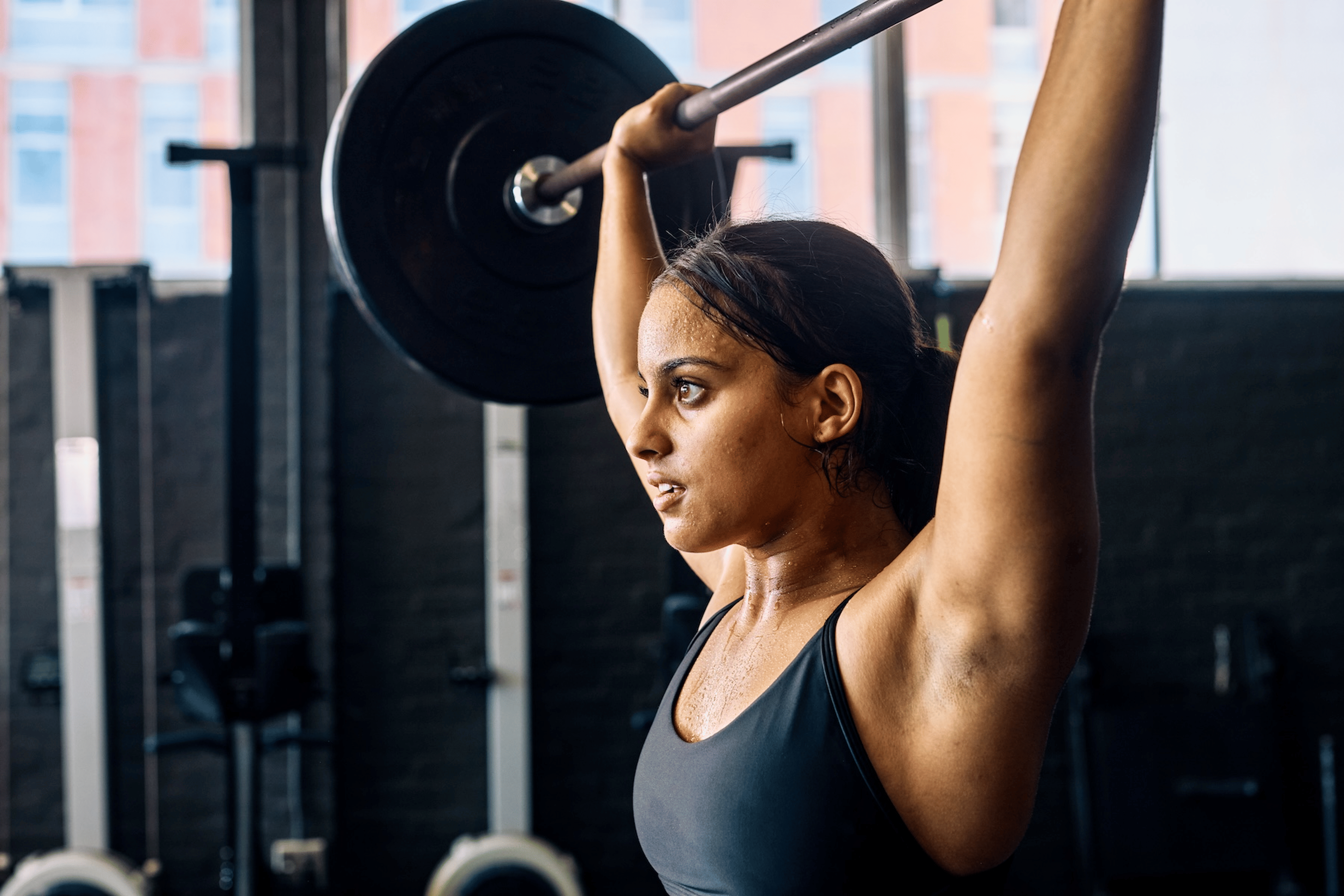 A woman doing an overhead press with a barbell in the gym.