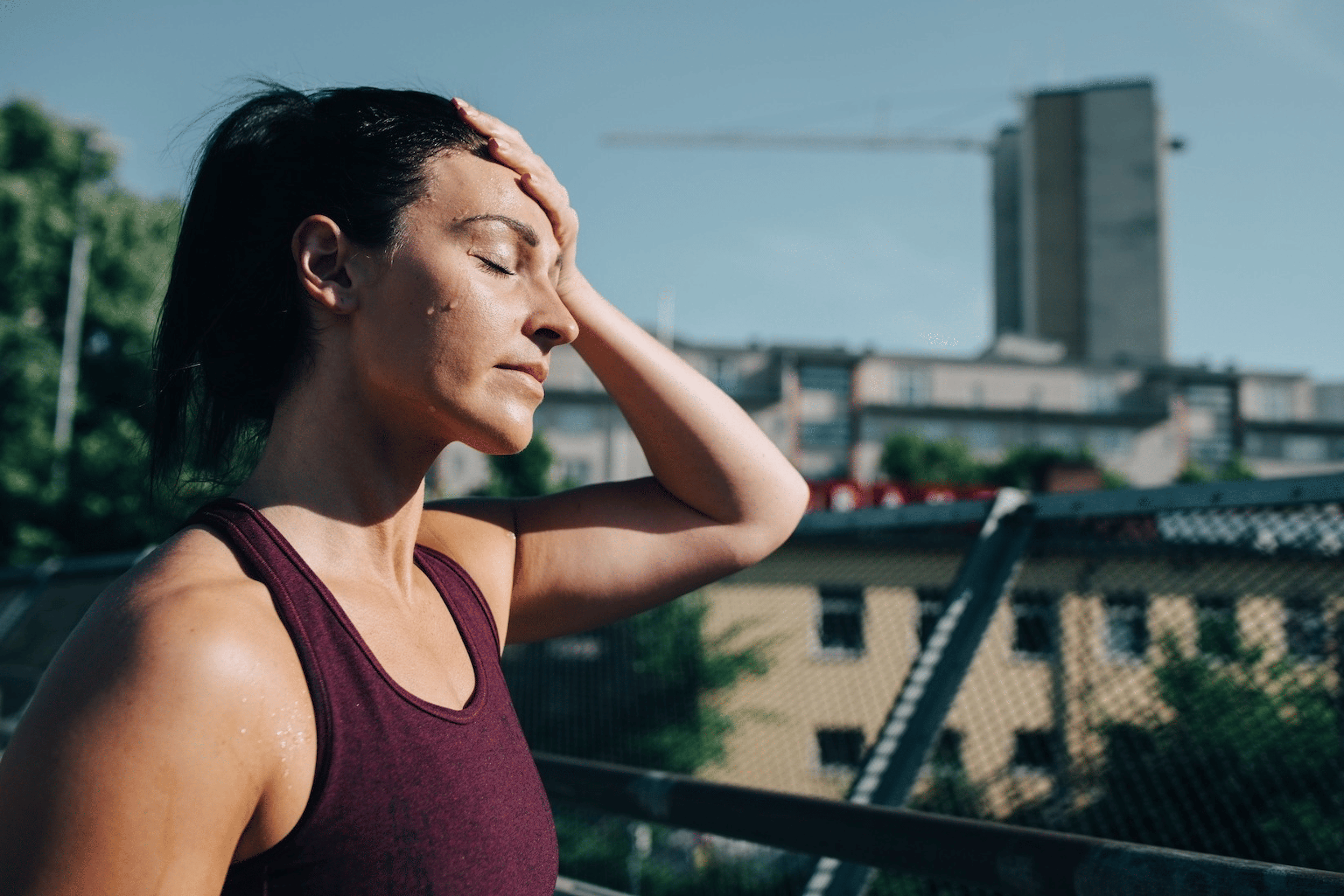A woman exercising in the heat. She's sweating with her hand on her forehead while walking outdoors.