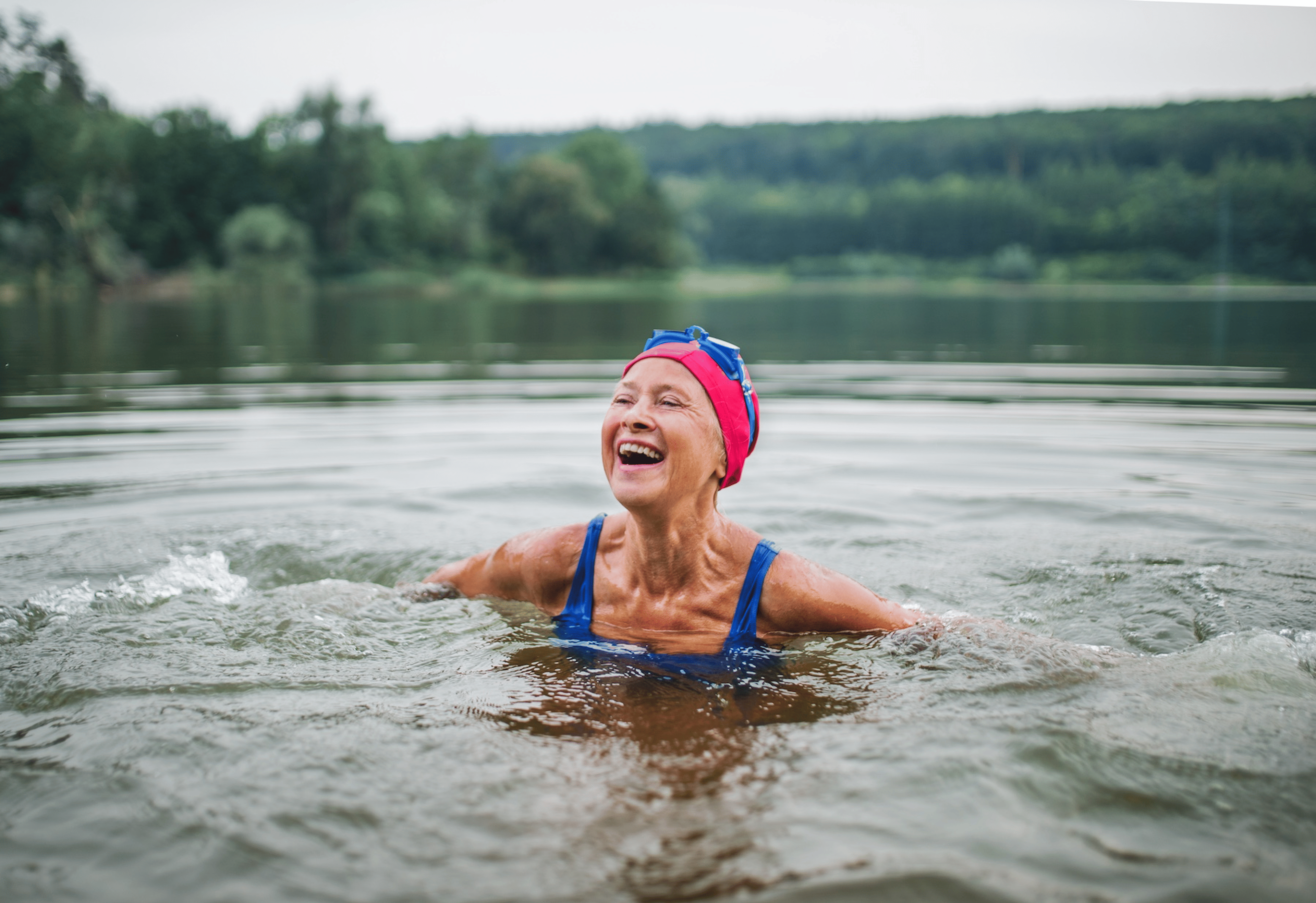 An older woman prioritizing her healthspan by joyfully swimming in an outdoor lake.