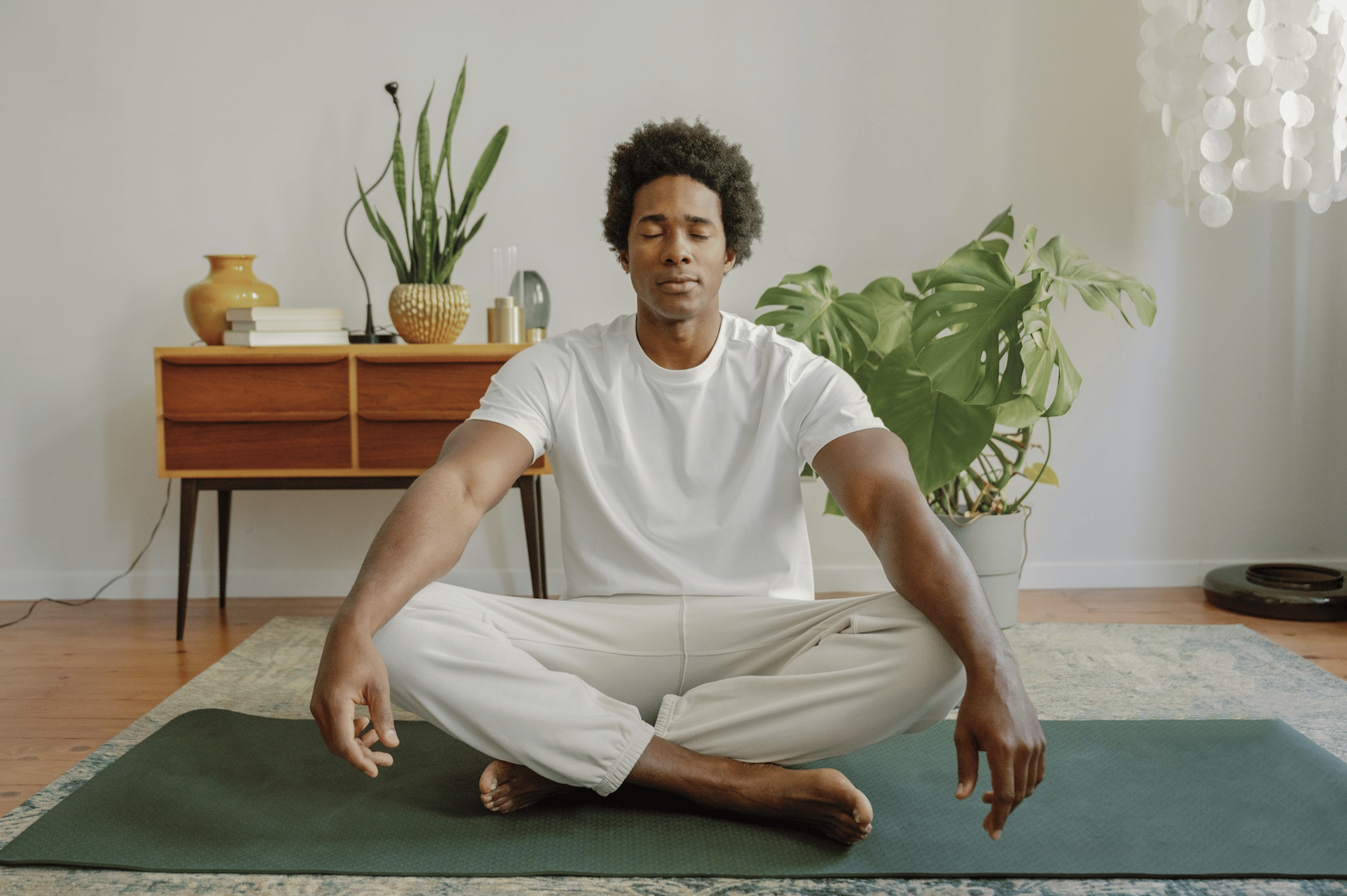 A man meditating with his eyes closed. He's sitting criss-cross on a yoga mat with his arms resting on his knees.
