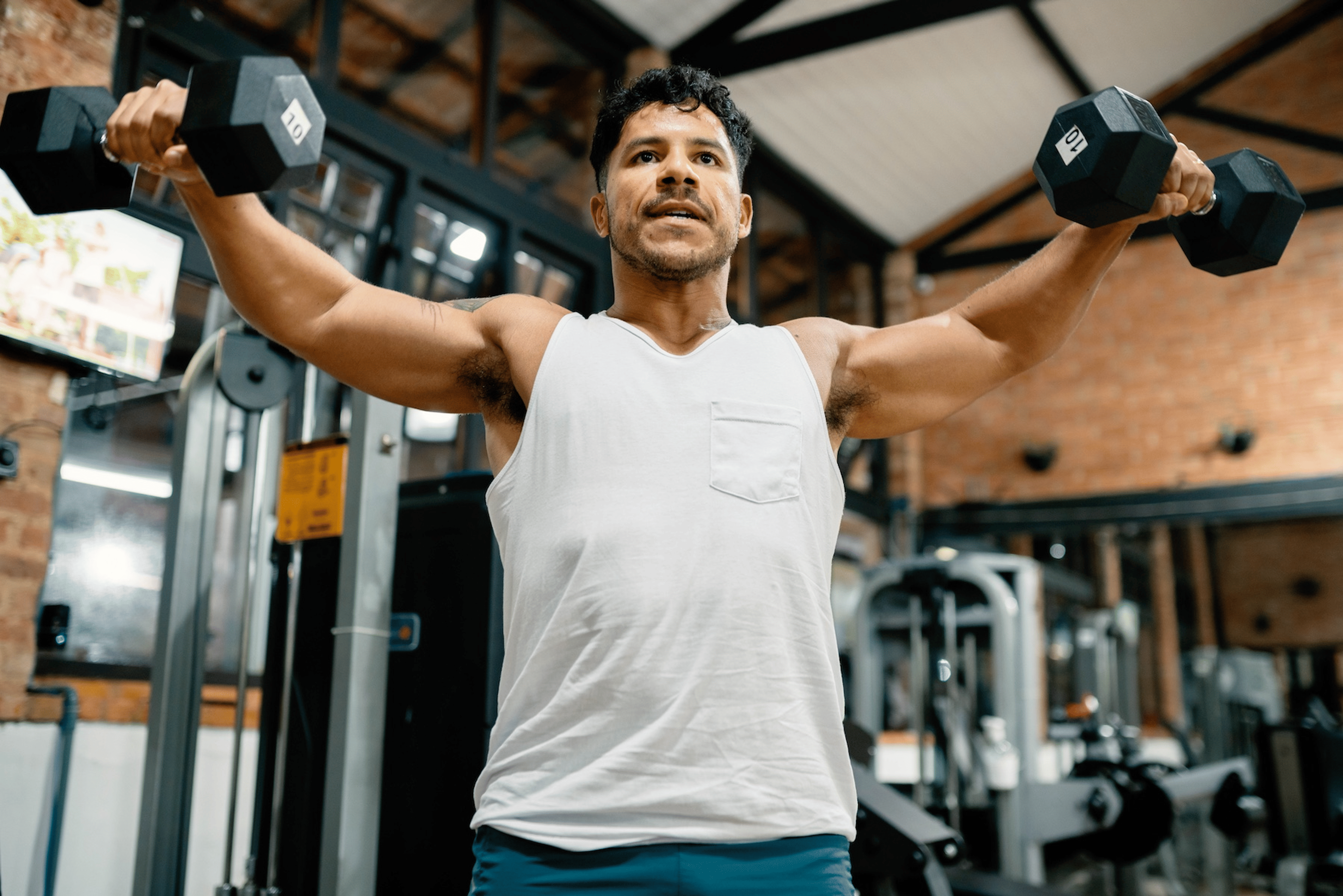 A man in the gym lifting dumbbells to exercise his shoulders.