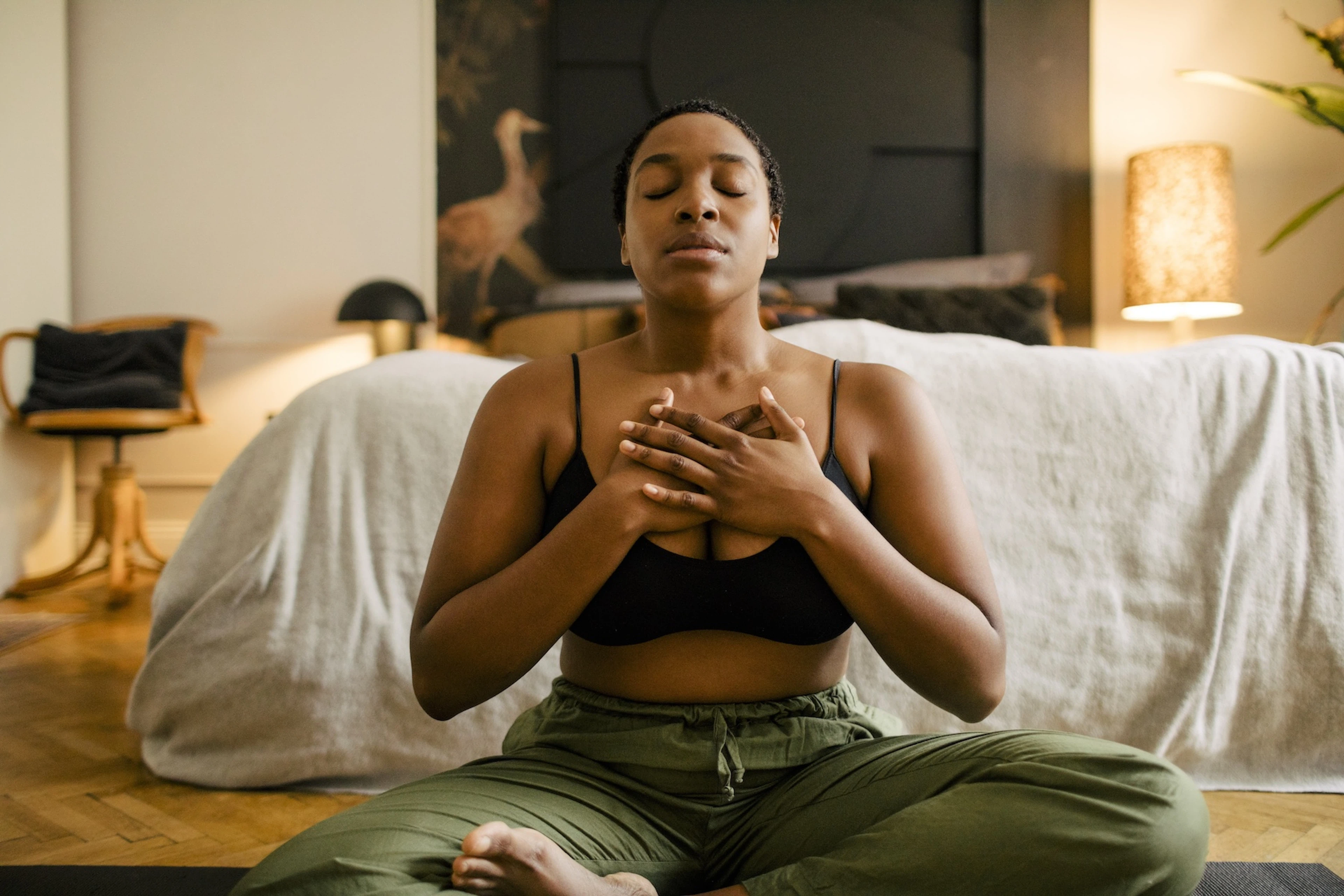 A woman practicing gratitude meditation at home. She's sitting down with her hands on her chest.
