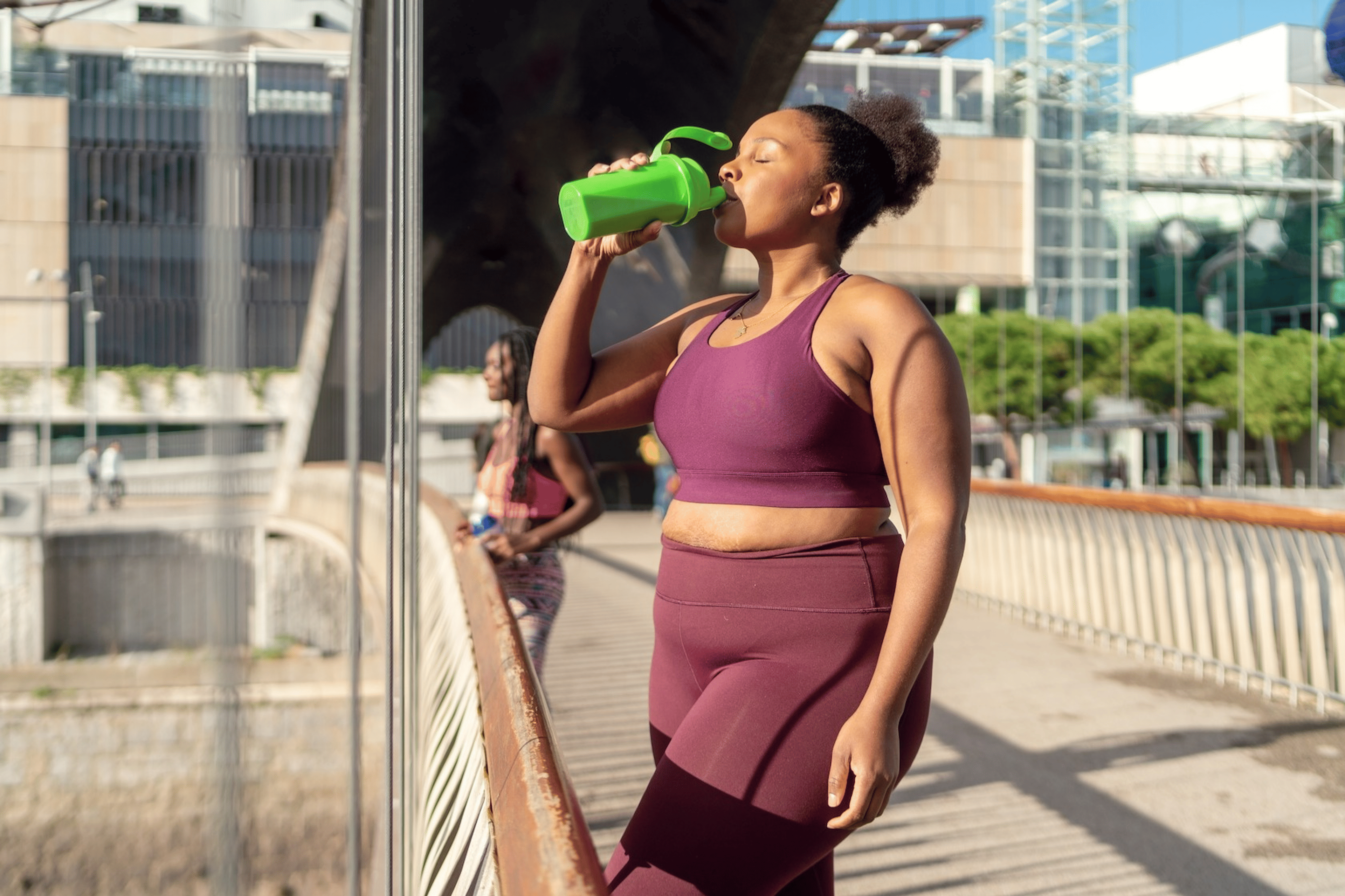 A woman drinking a smoothie after an outdoor cardio workout.