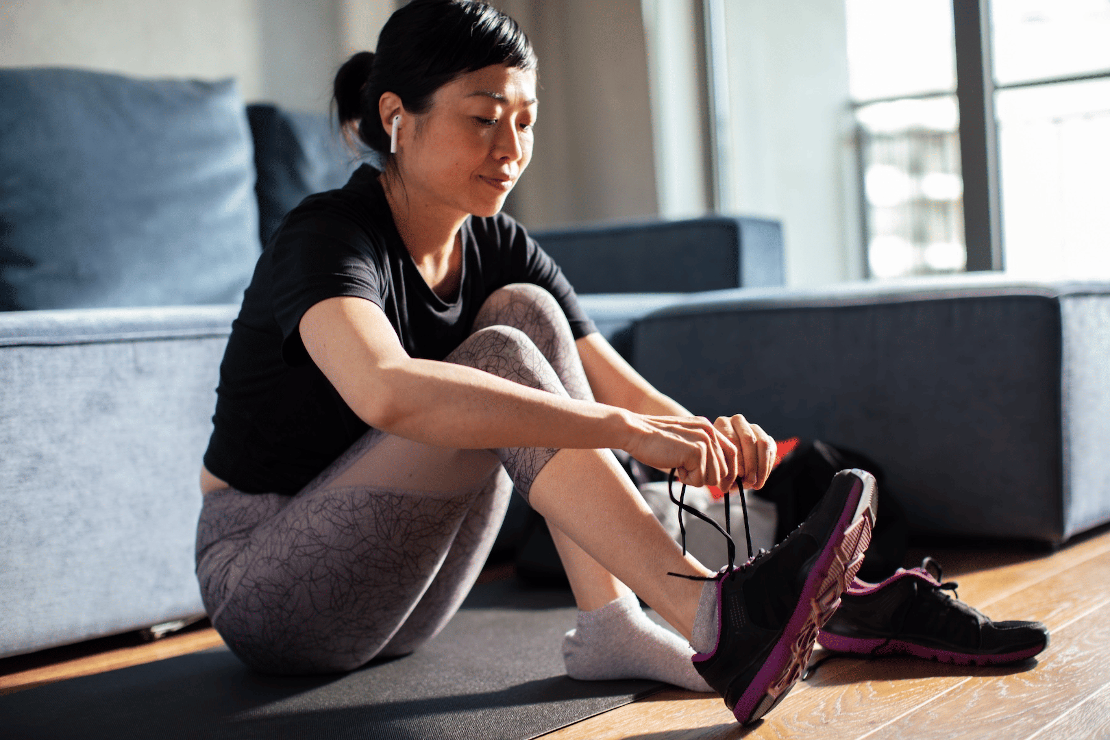 A woman sitting down at home and tying her shoes in a way that doesn't make her feet go numb while running.