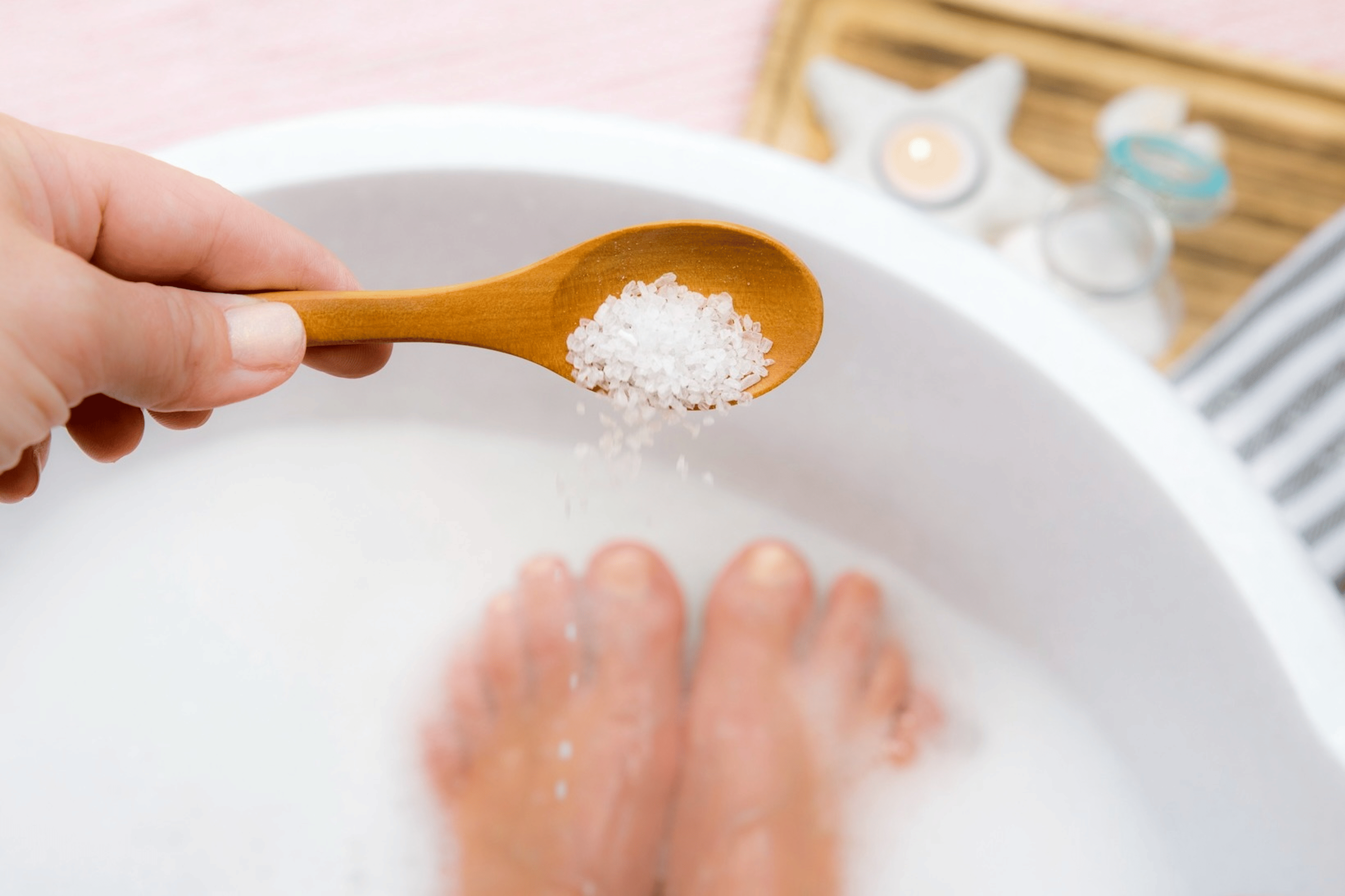 A hand pouring Epsom salt into a foot bath.