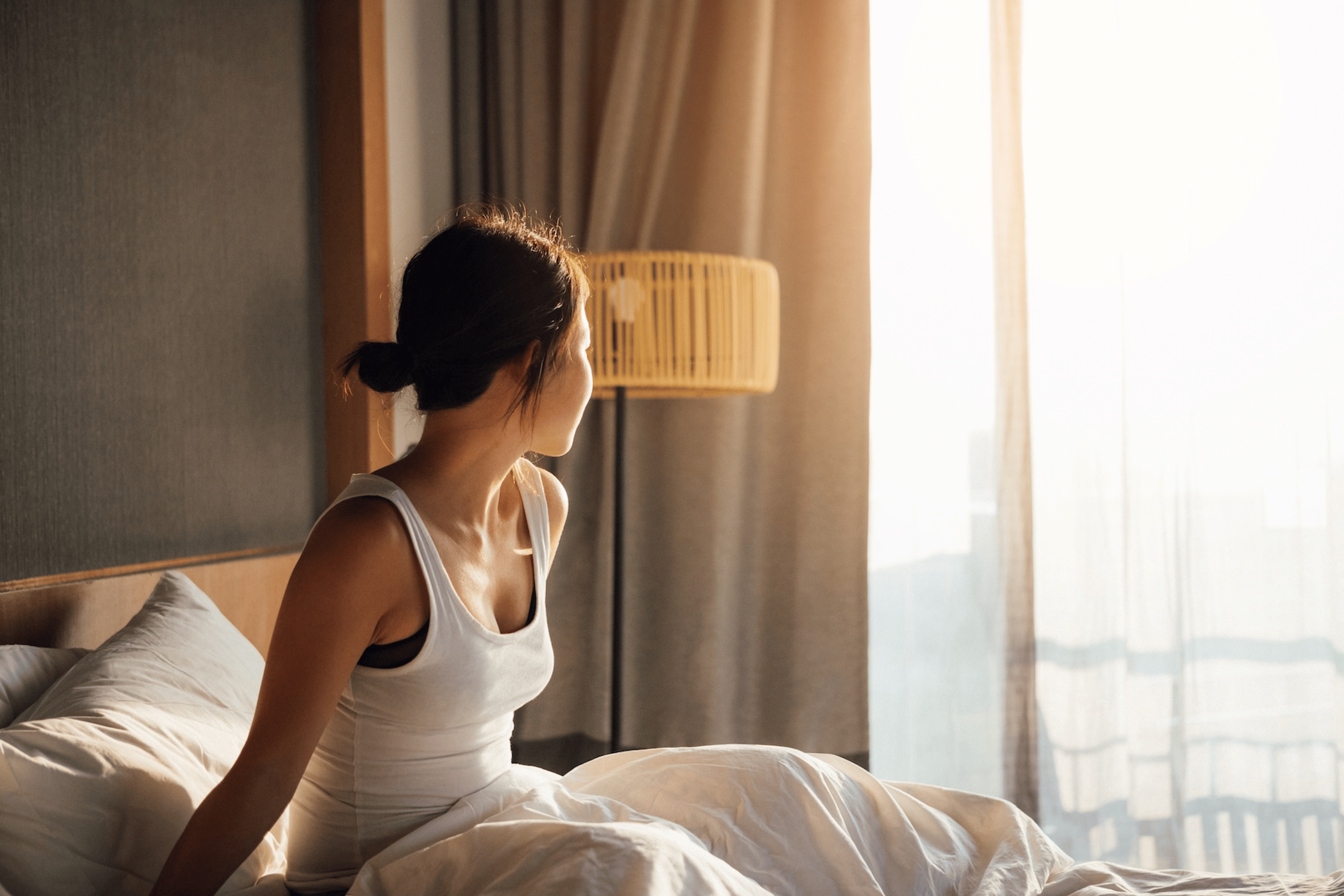 A woman waking up early. She's sitting up in bed and looking out the window.