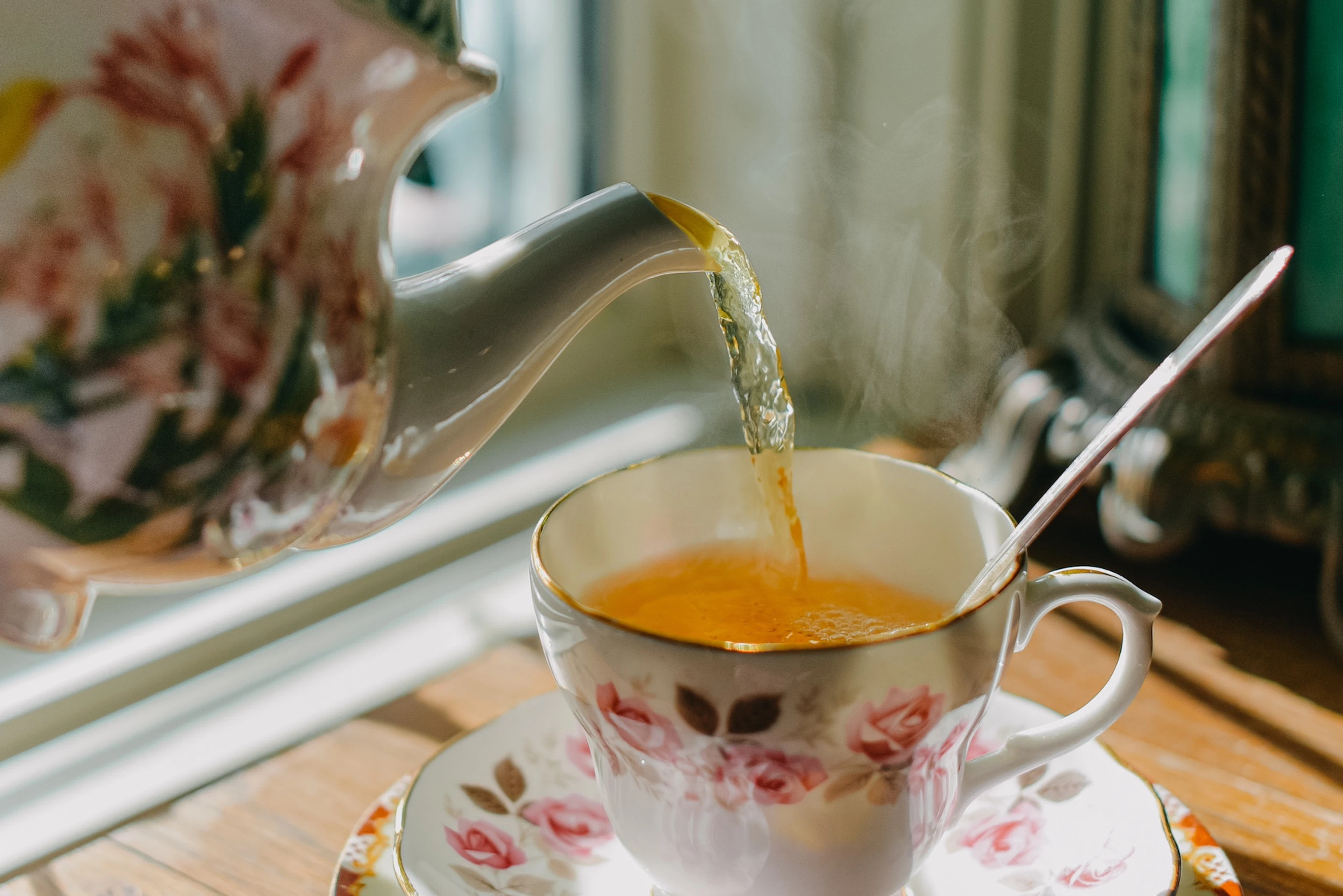 A tea pot pouring tea, a hydrating food, into a floral tea cup.