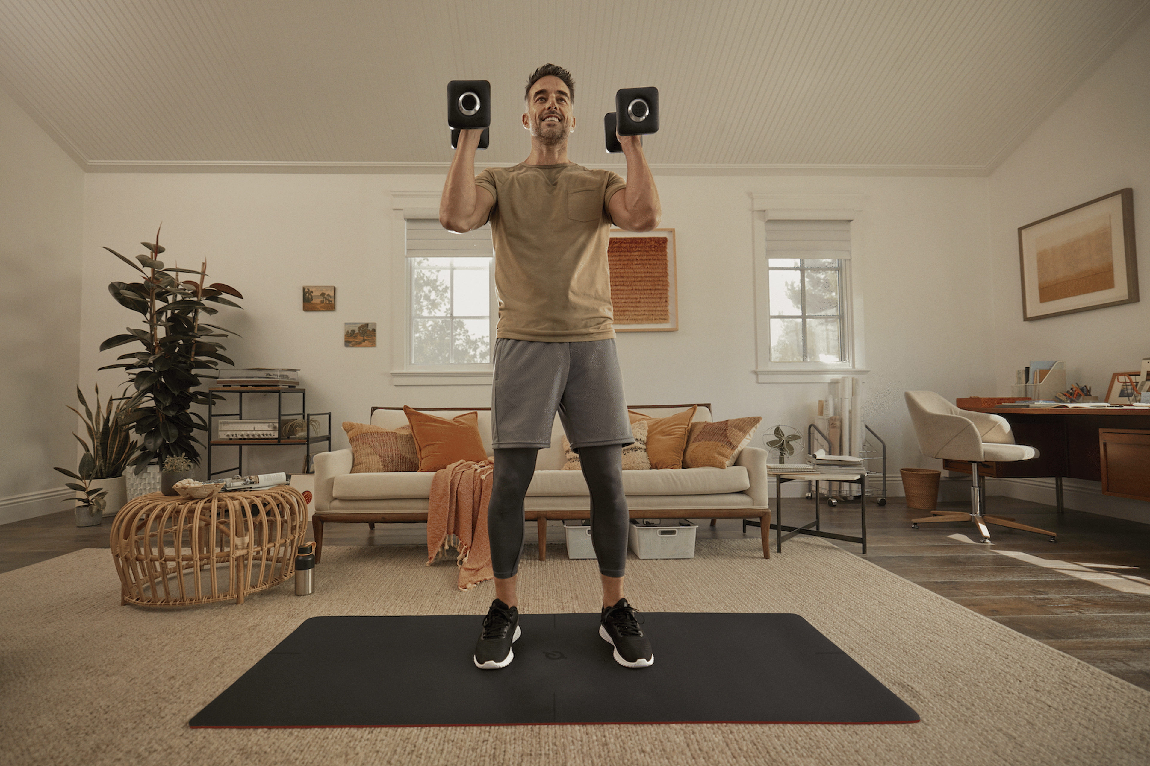 Man holds dumbbells while doing hamstring exercises during a Peloton strength workout at home