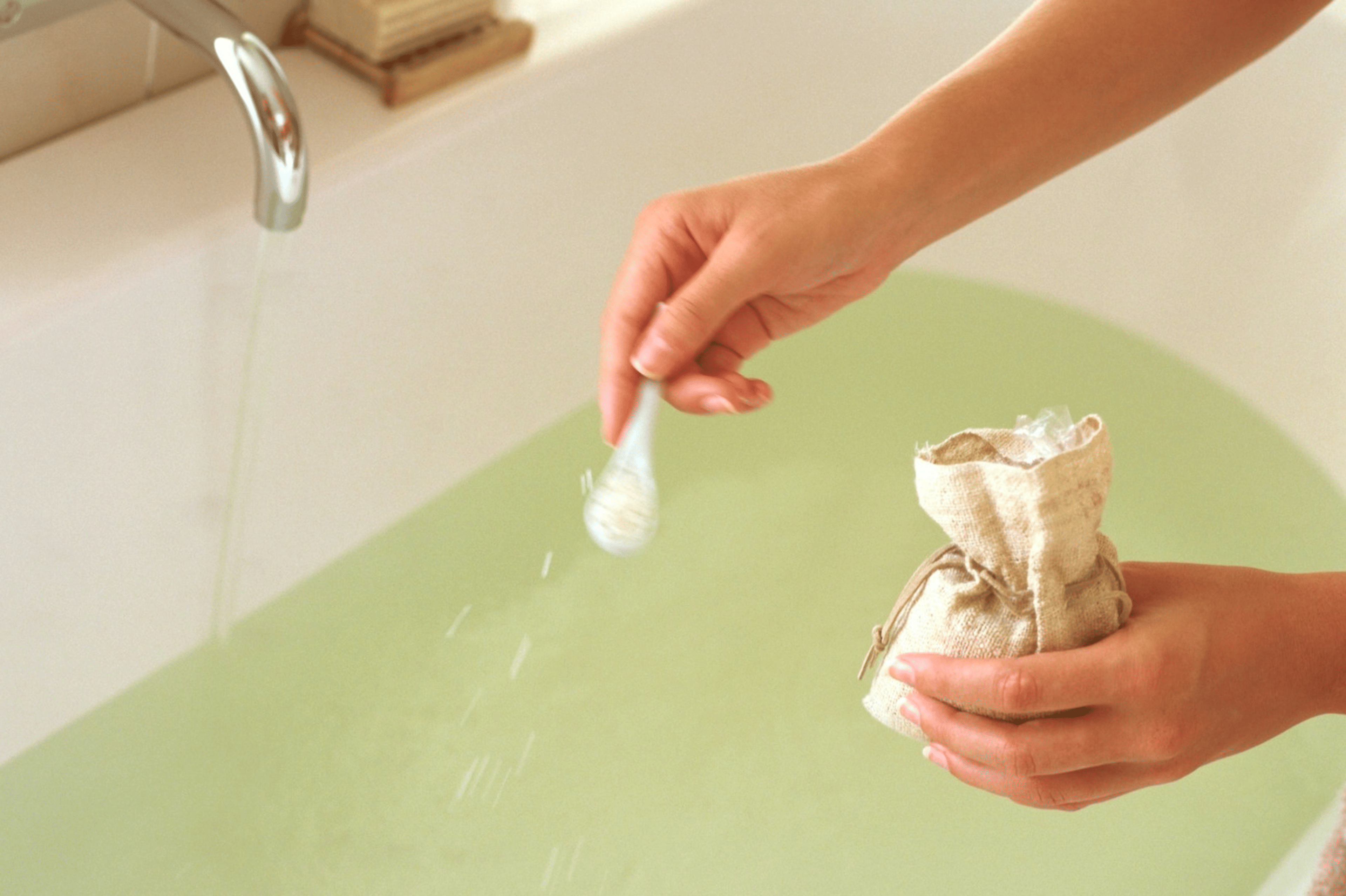 A close-up photo of a person sprinkling Epsom salt into a bath.