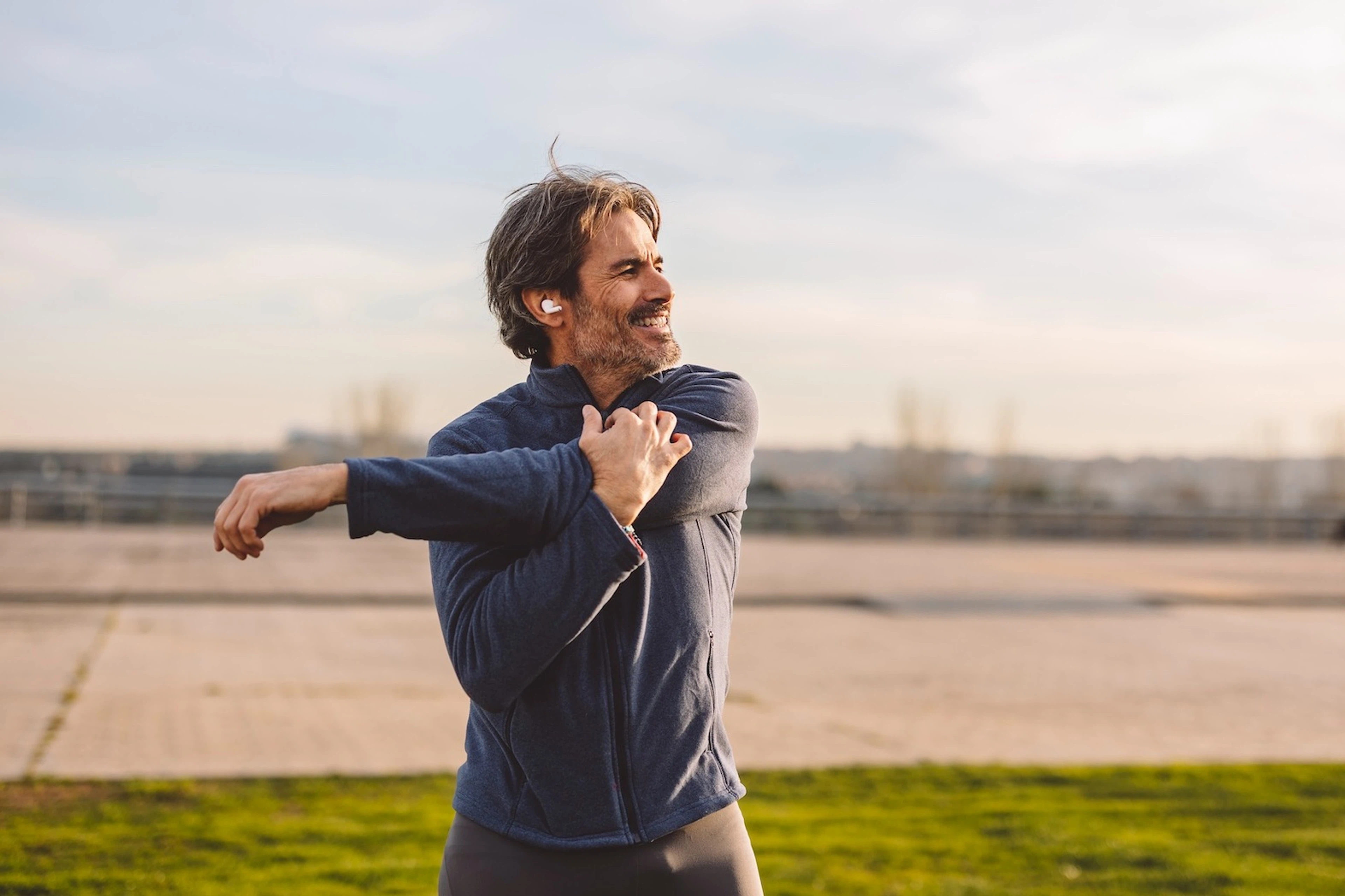 A happy, mature man stretching his arms before exercising outside.