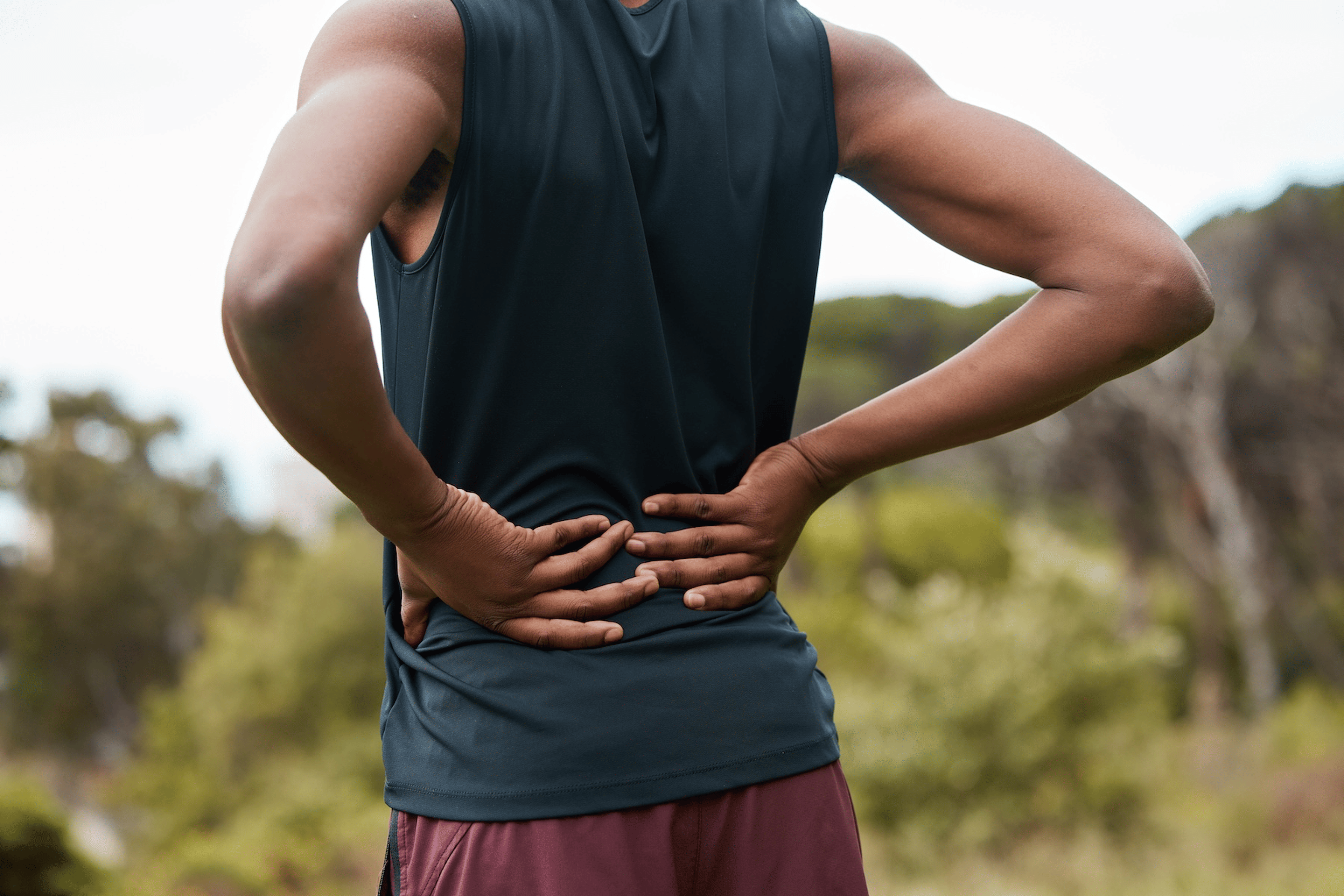 A close-up photo of a runner with their hands on their lower back, experiencing pain.