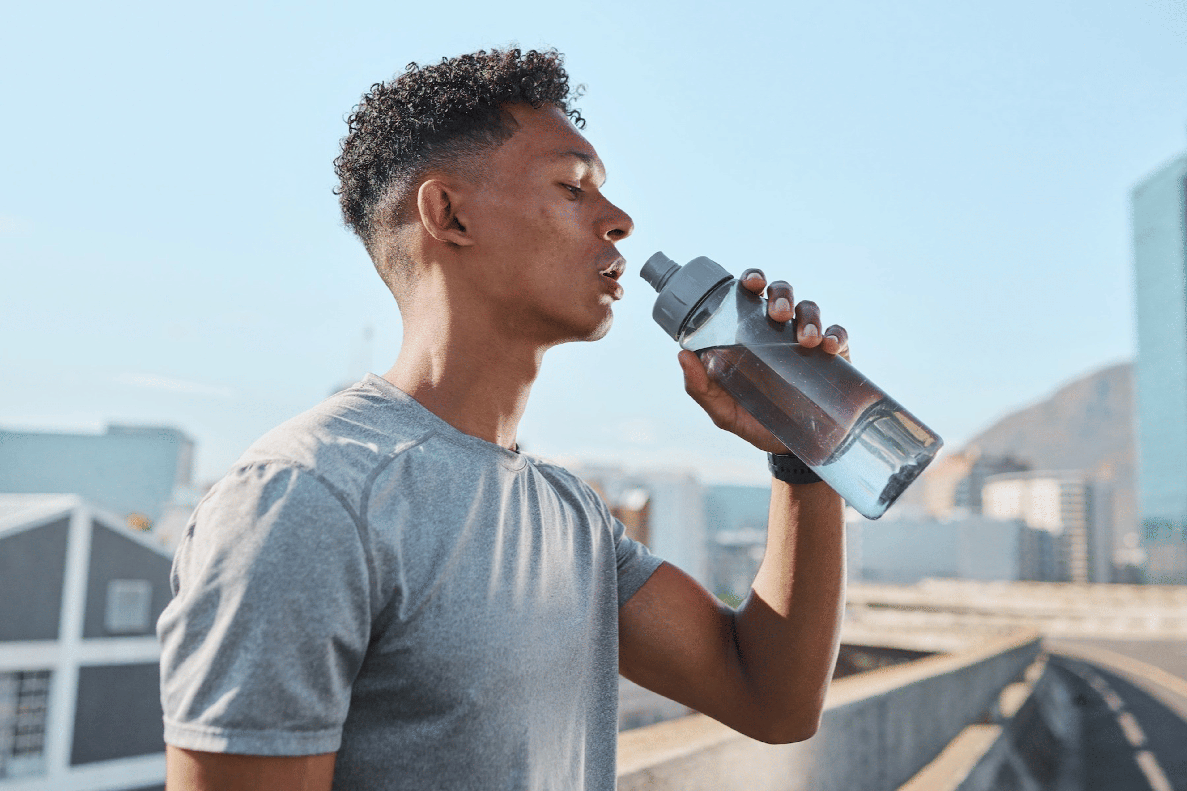 A man exercising in the heat, pausing for a sip of water from his water bottle.