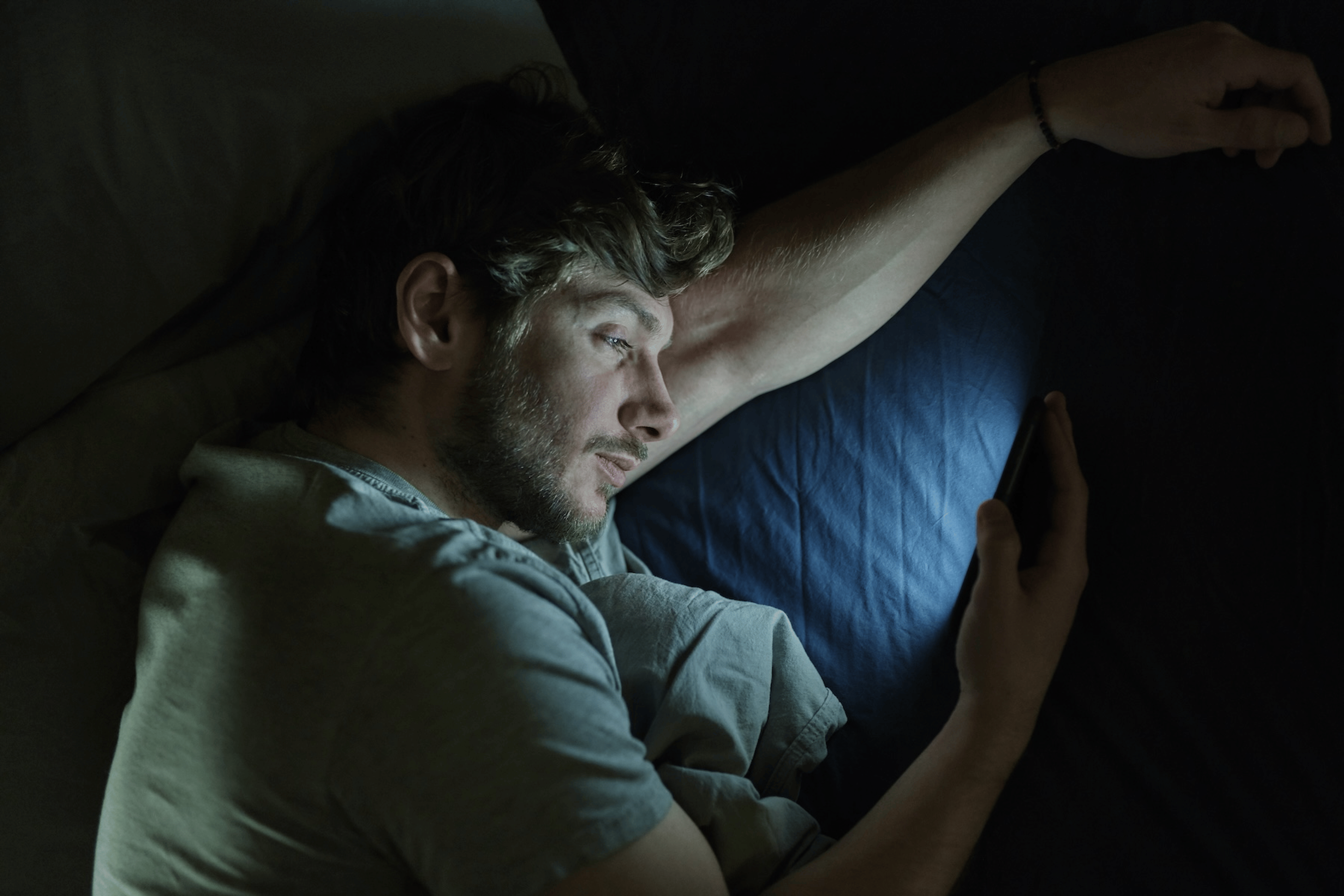 A man lying in bed and staring at his phone at night.
