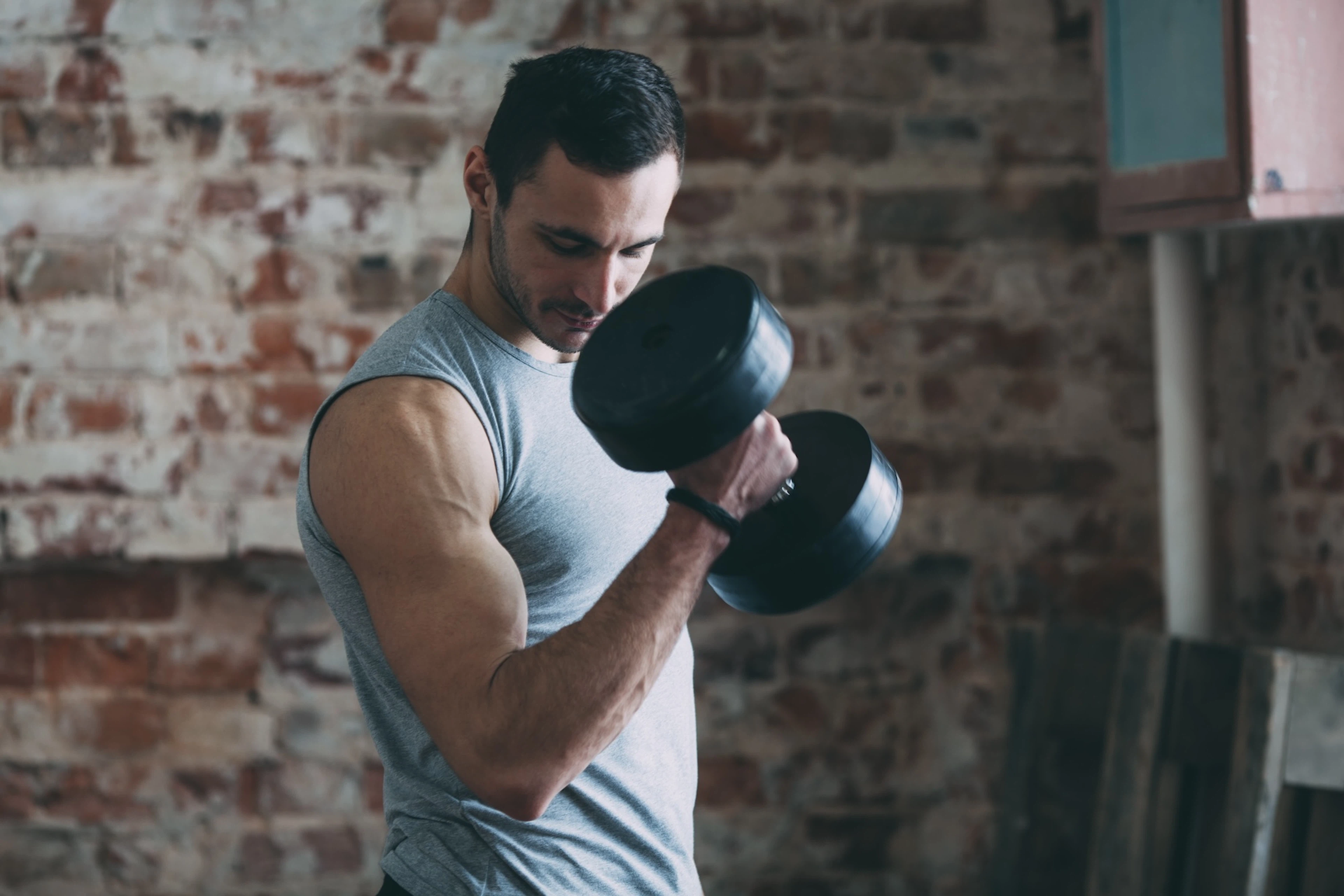 A man doing a single-arm bicep curl with a dumbbell. He is looking at his arm to enhance the mind-muscle connection.