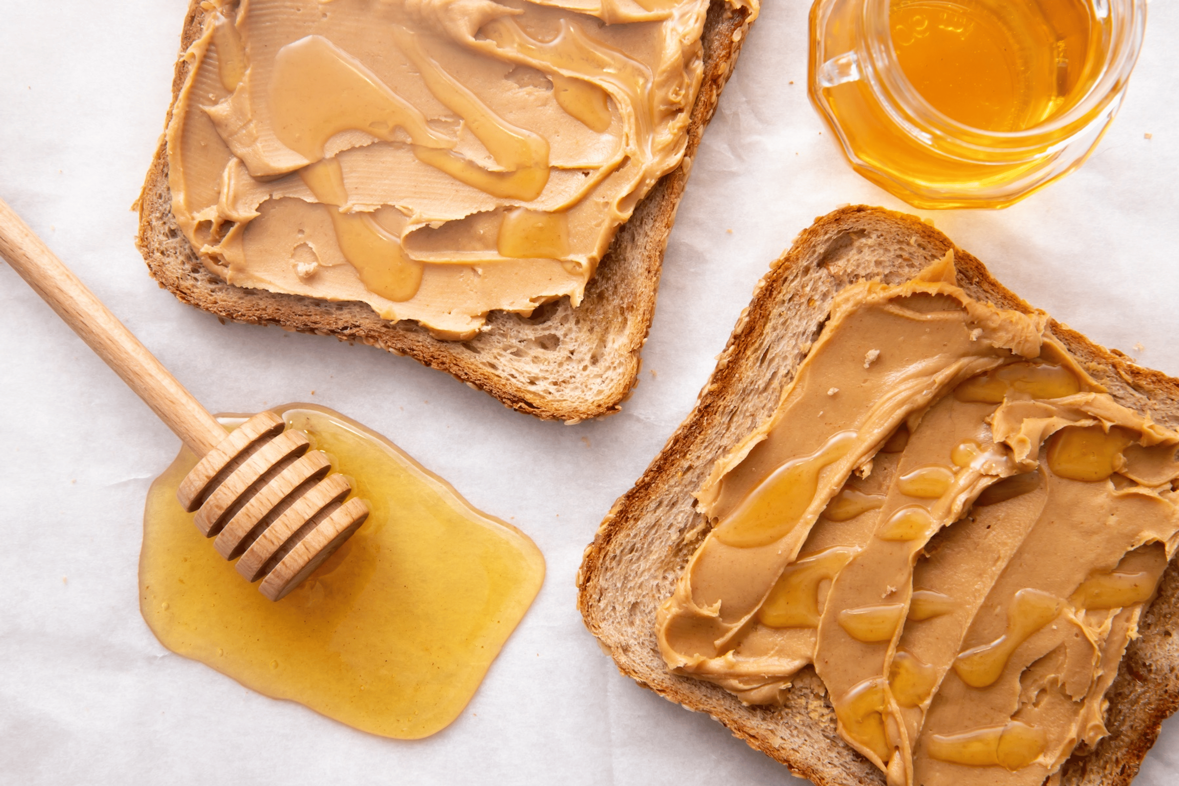 A honey stick sitting near two slices of peanut butter toast that also have honey on them.