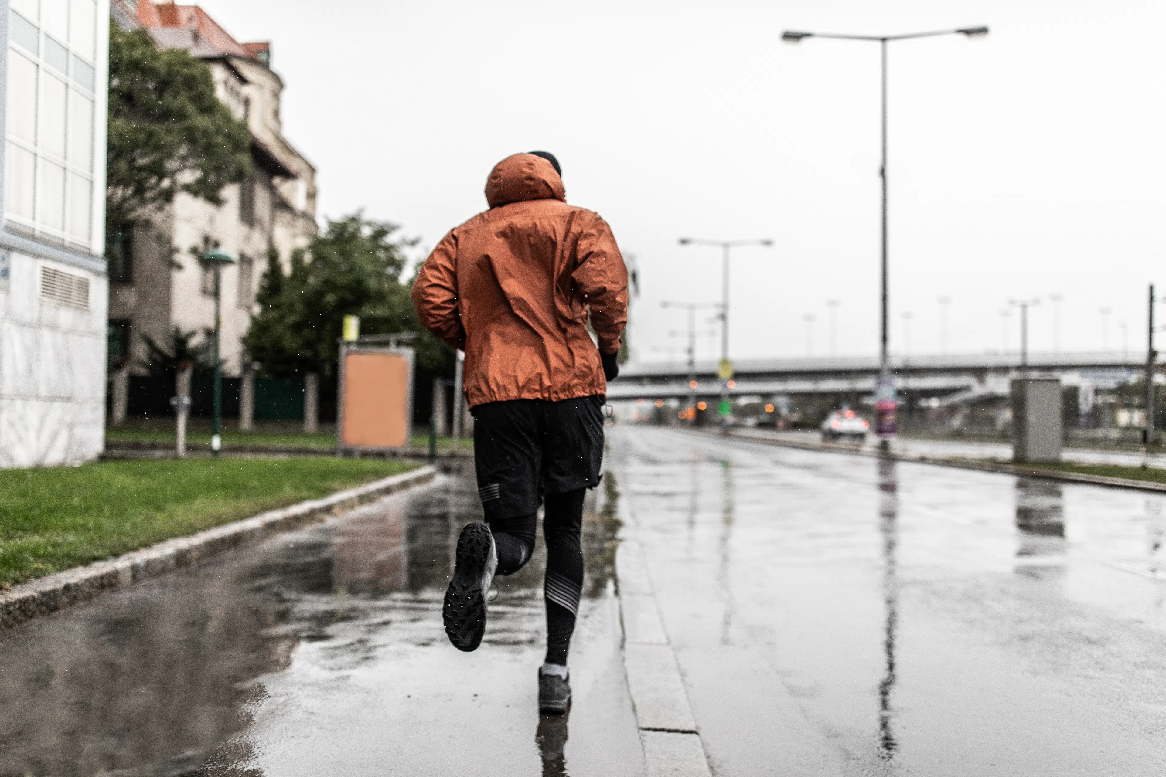 Man running in the rain through a city in an orange rain jacket