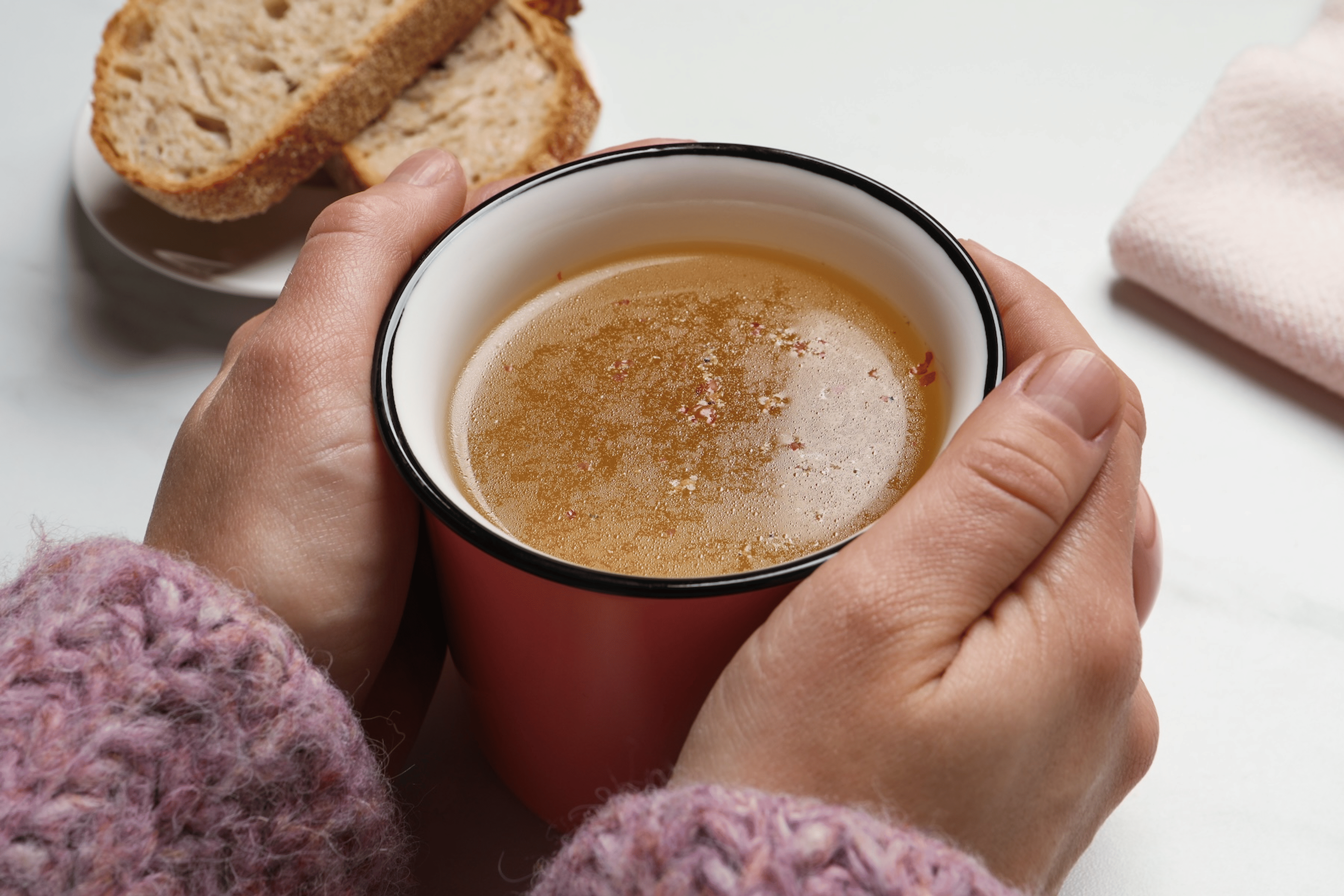 Close-up photo of a pair of hands holding a cup of bone broth.