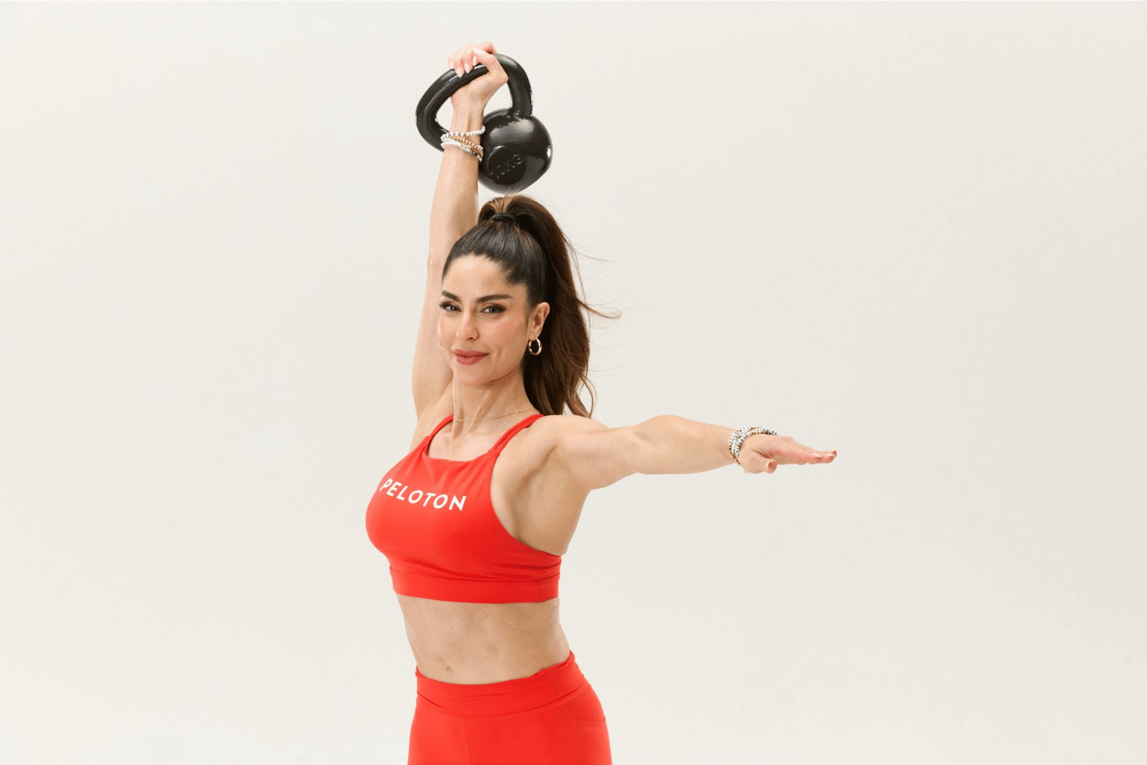 Peloton instructor Assal Arian holding a kettlebell above her head