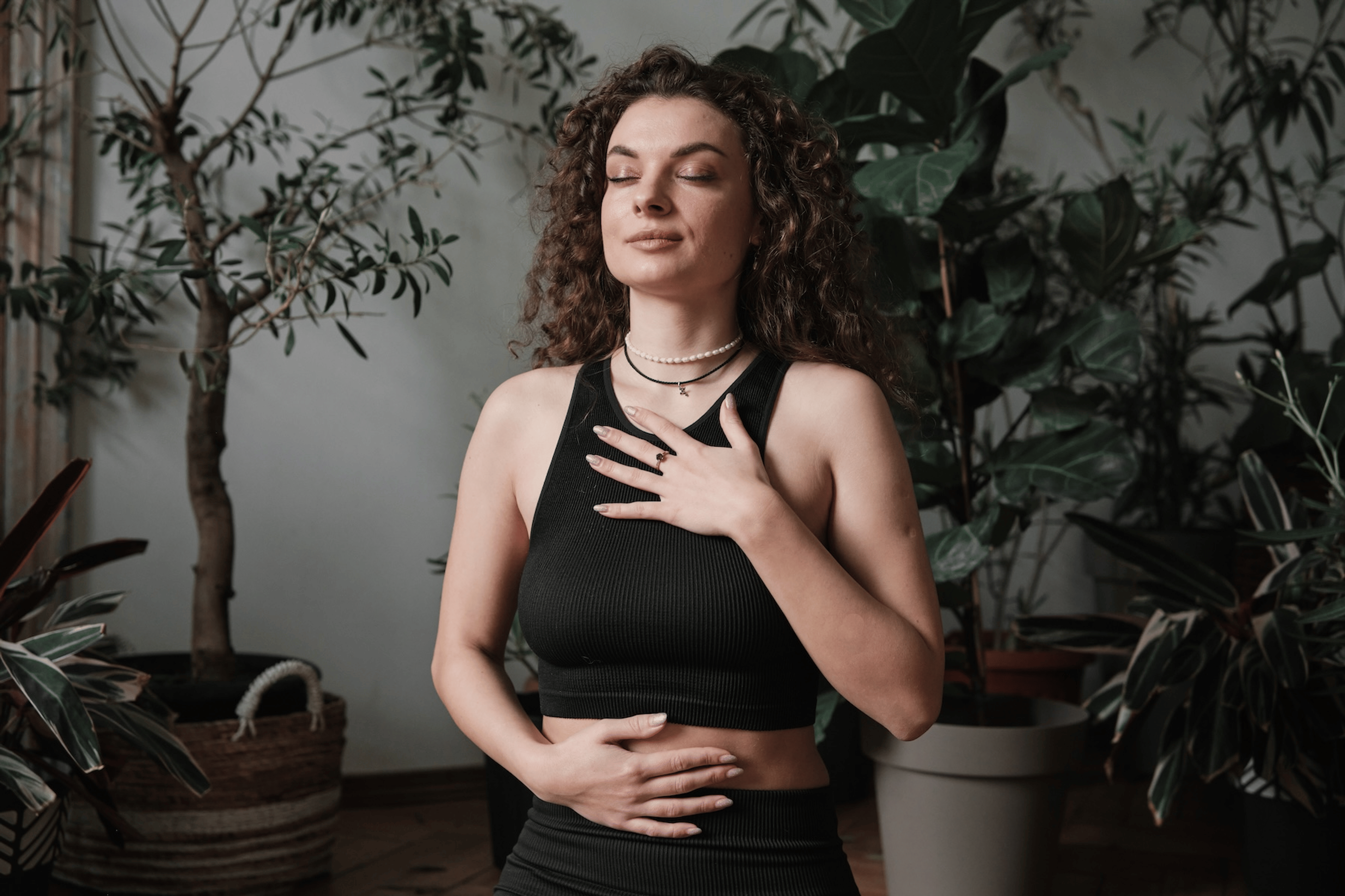 A woman practicing belly breathing. She is sitting tall with one hand on her chest and one hand on her belly, her eyes closed.
