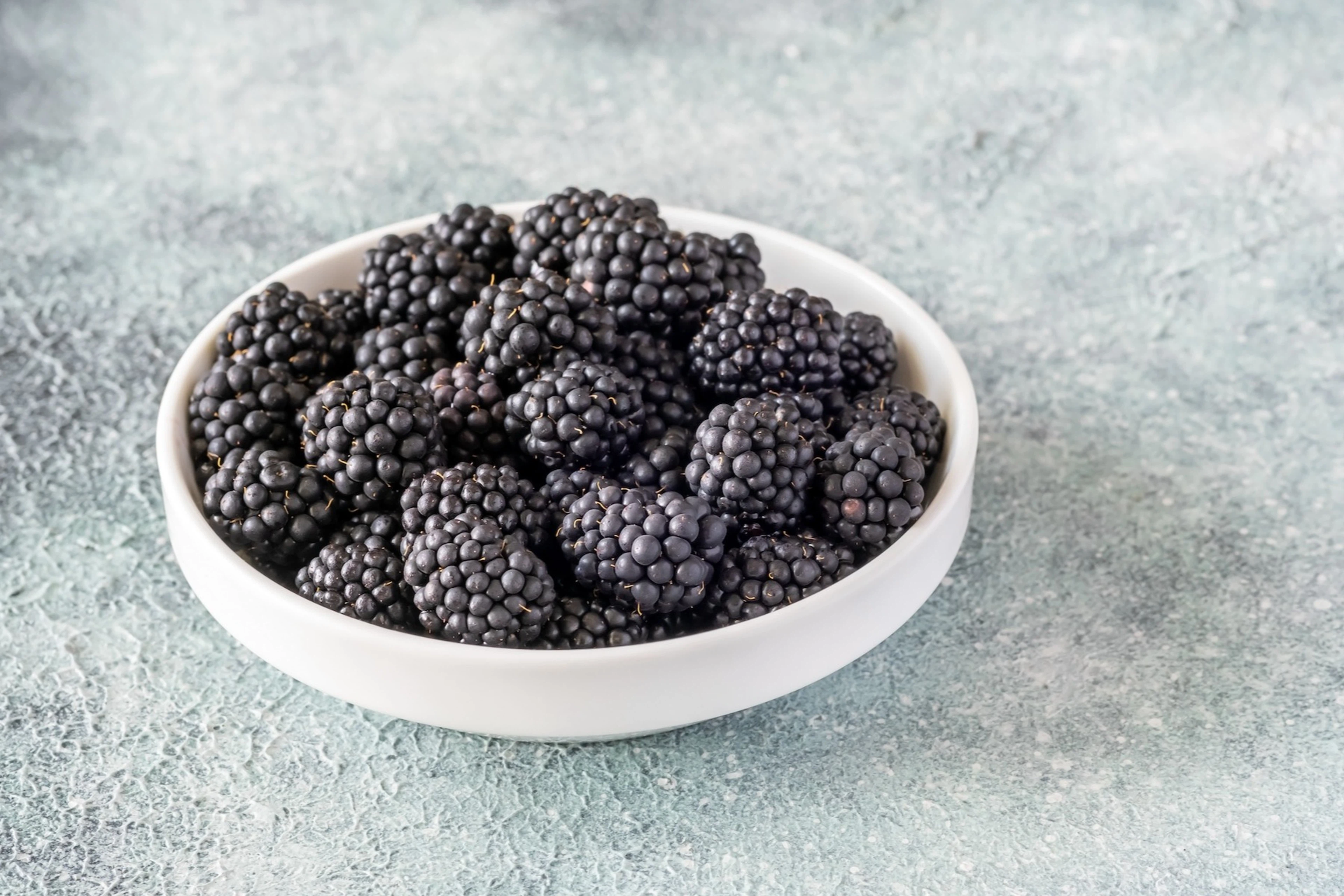 A white bowl of blackberries (which are high-protein fruits) sitting on a table.