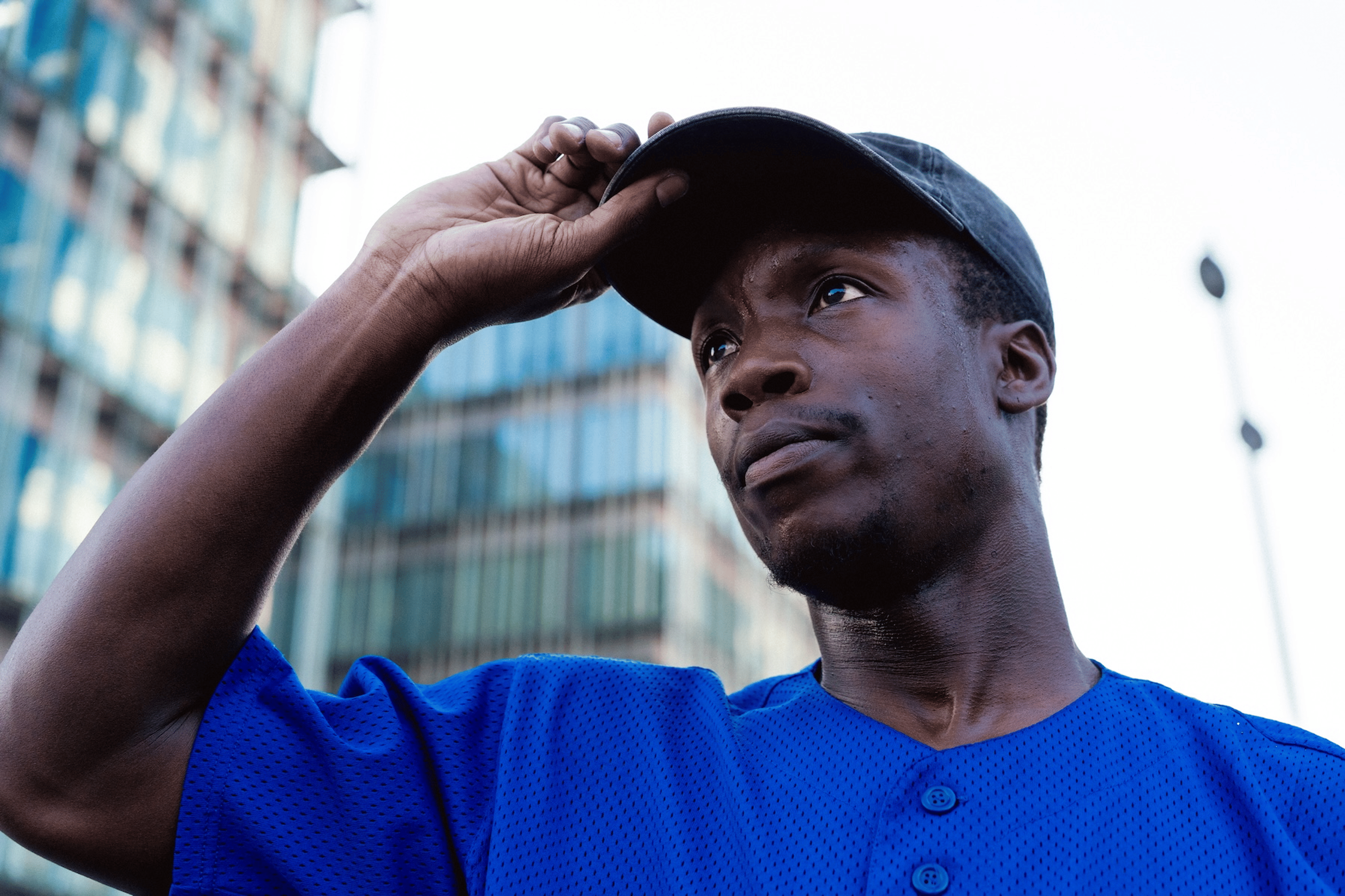 A sweaty man adjusting his baseball hat while he stands outside and looks into the distance.