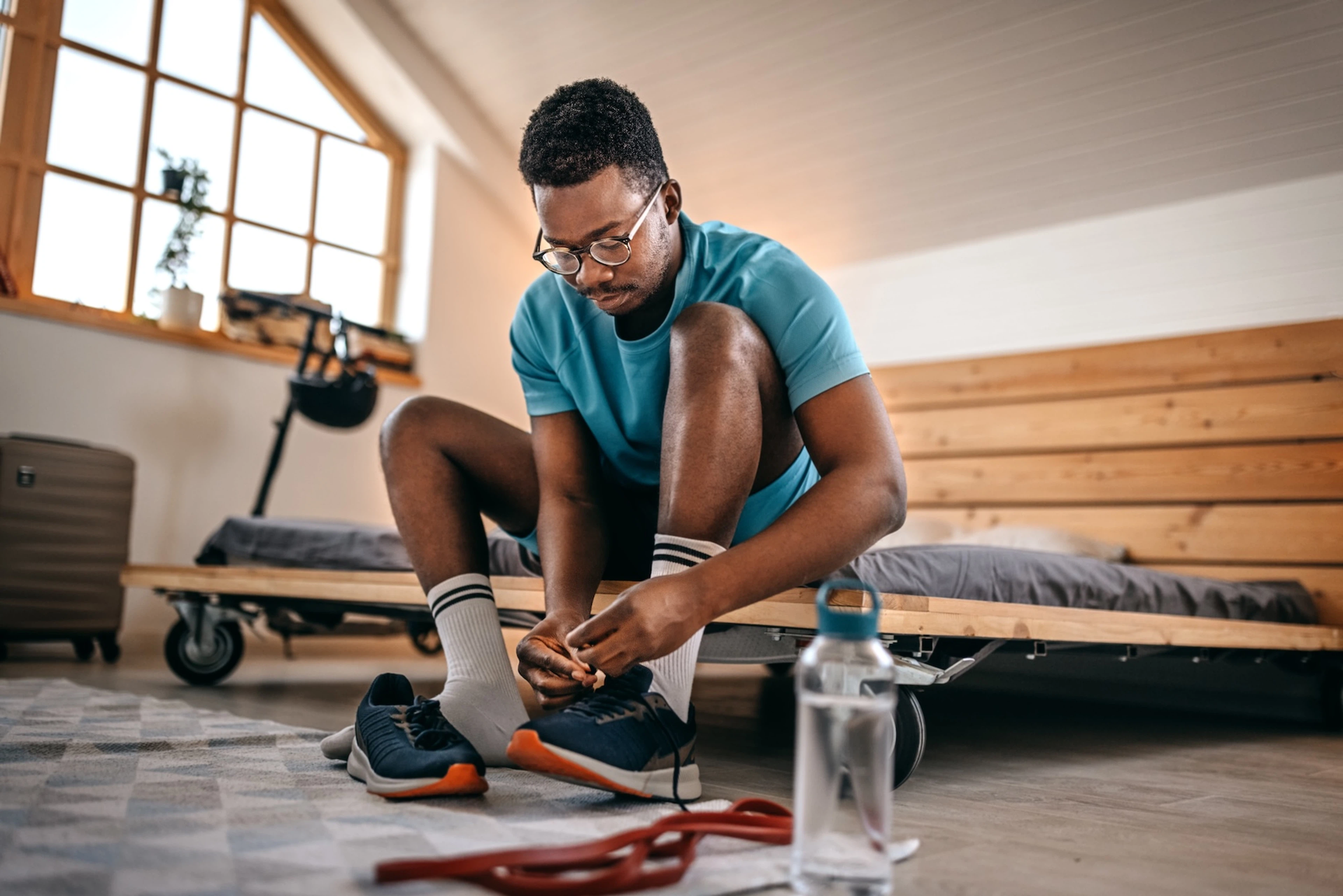 A man practicing self-discipline for exercise. He is sitting on his bed and tying his workout shoes before exercising, even if he may not feel like it. 
