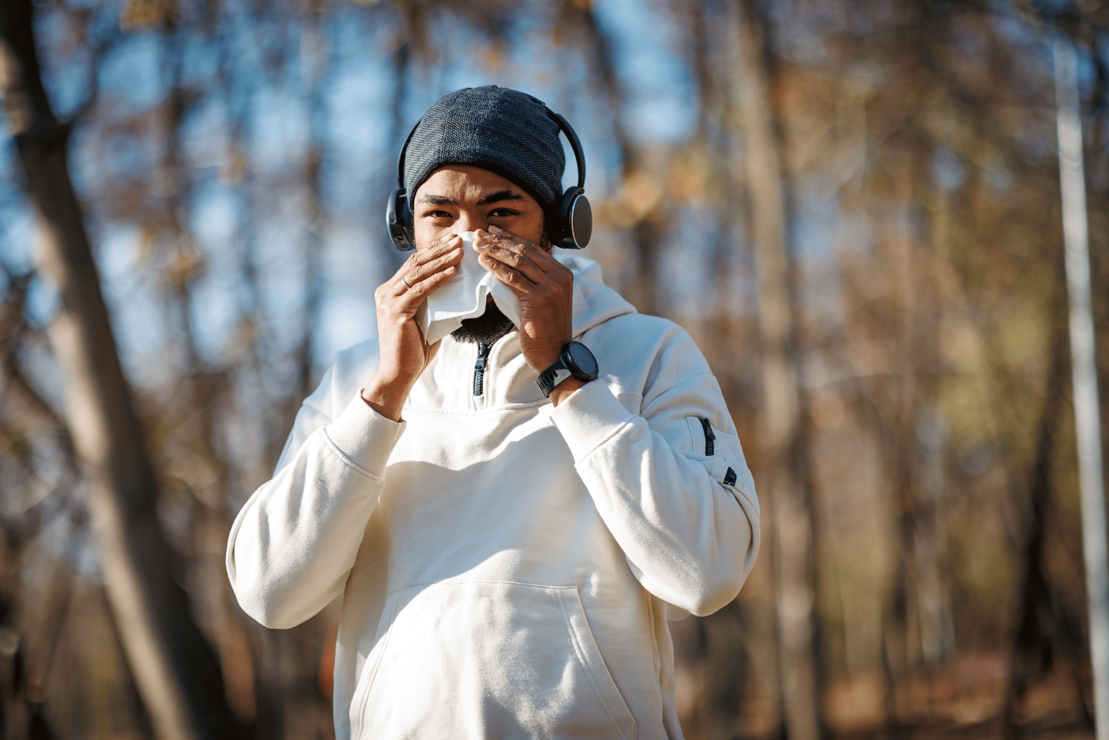 A man going on a run on a chilly day while stopping to blow his nose. He is running while sick.