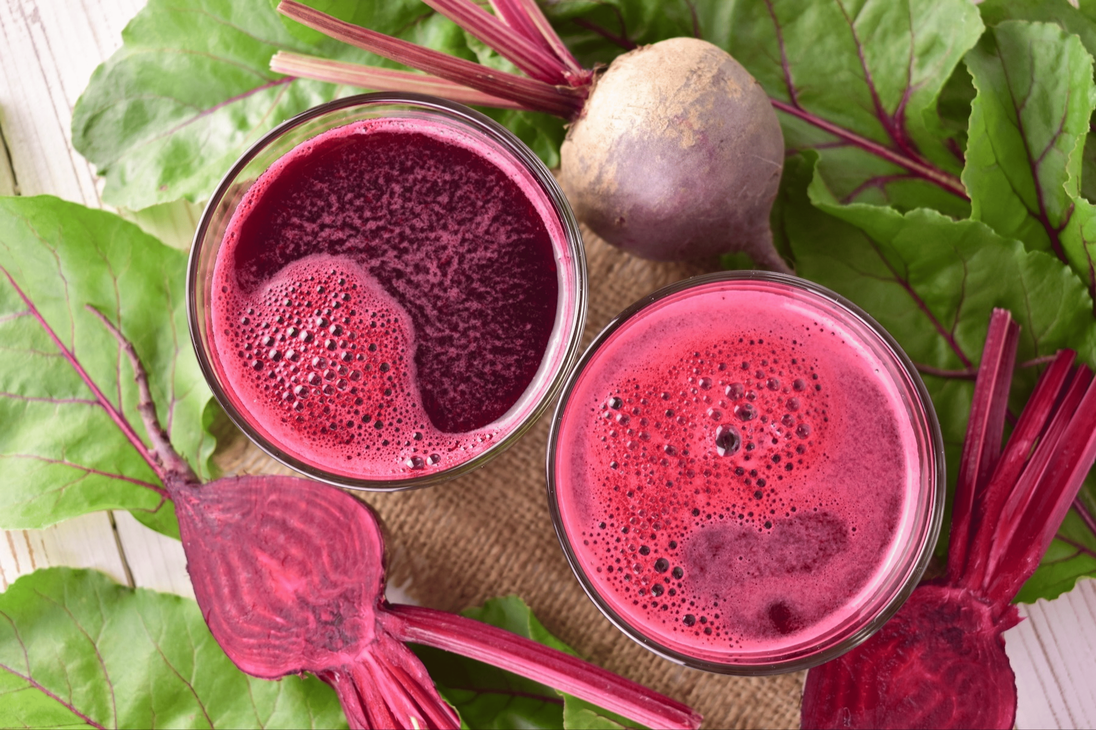 A bird's-eye view of two glasses of beet juice surrounded by whole beets.