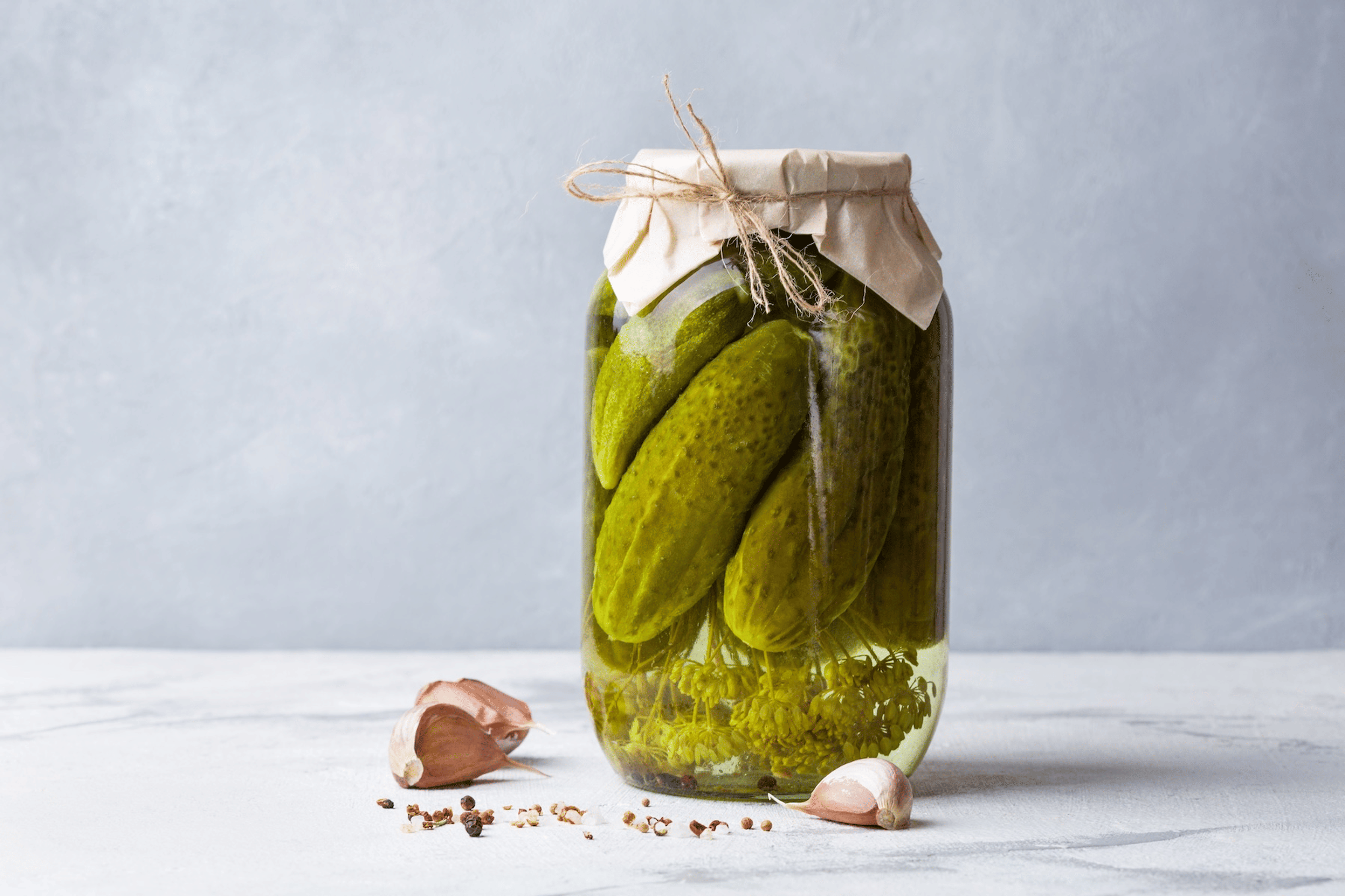 A glass jar of homemade pickles sitting on a counter. Learn more about pickle juice for cramps in this article.