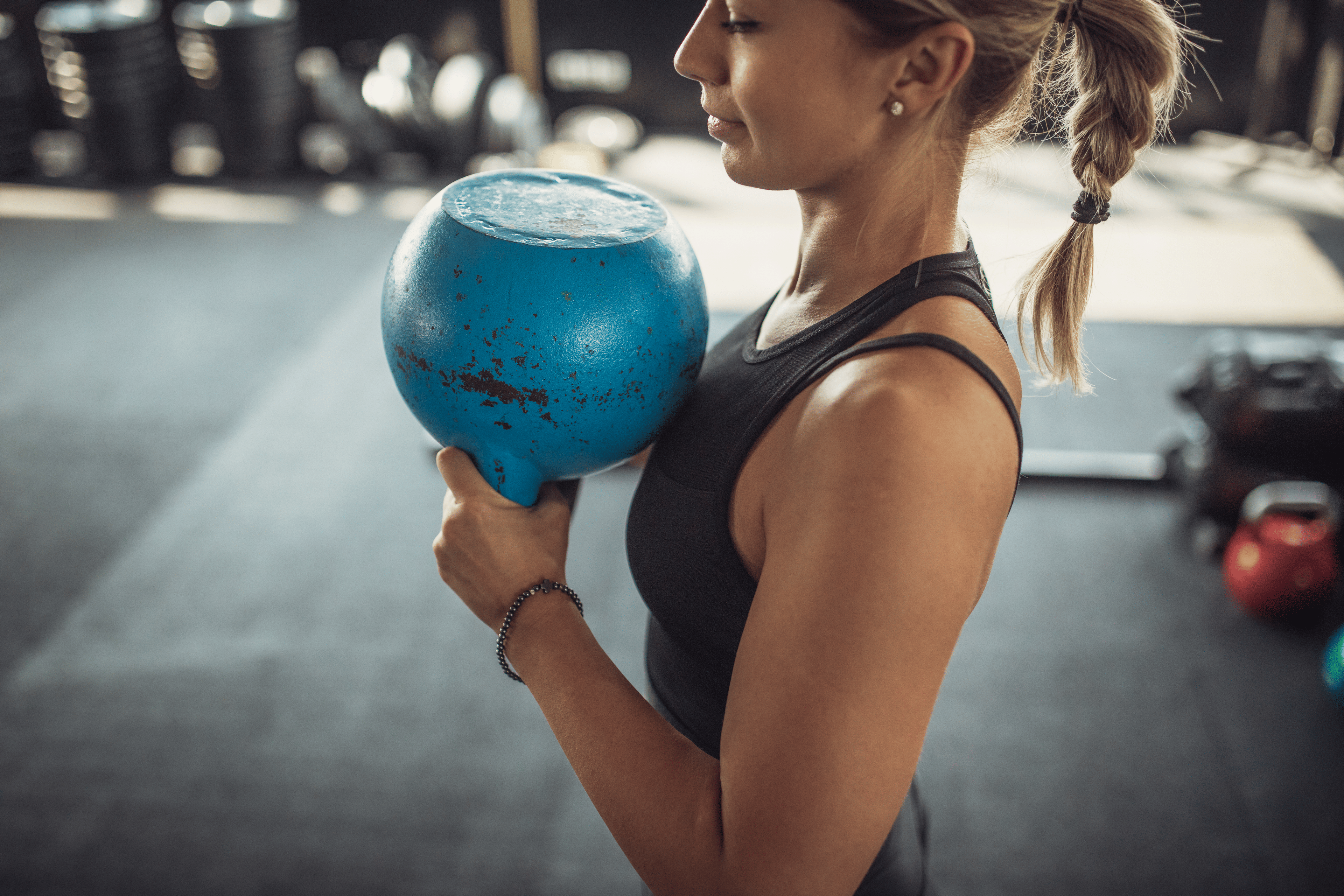 Woman doing the kettlebell halos exercise in a gym with a blue kettlebell.