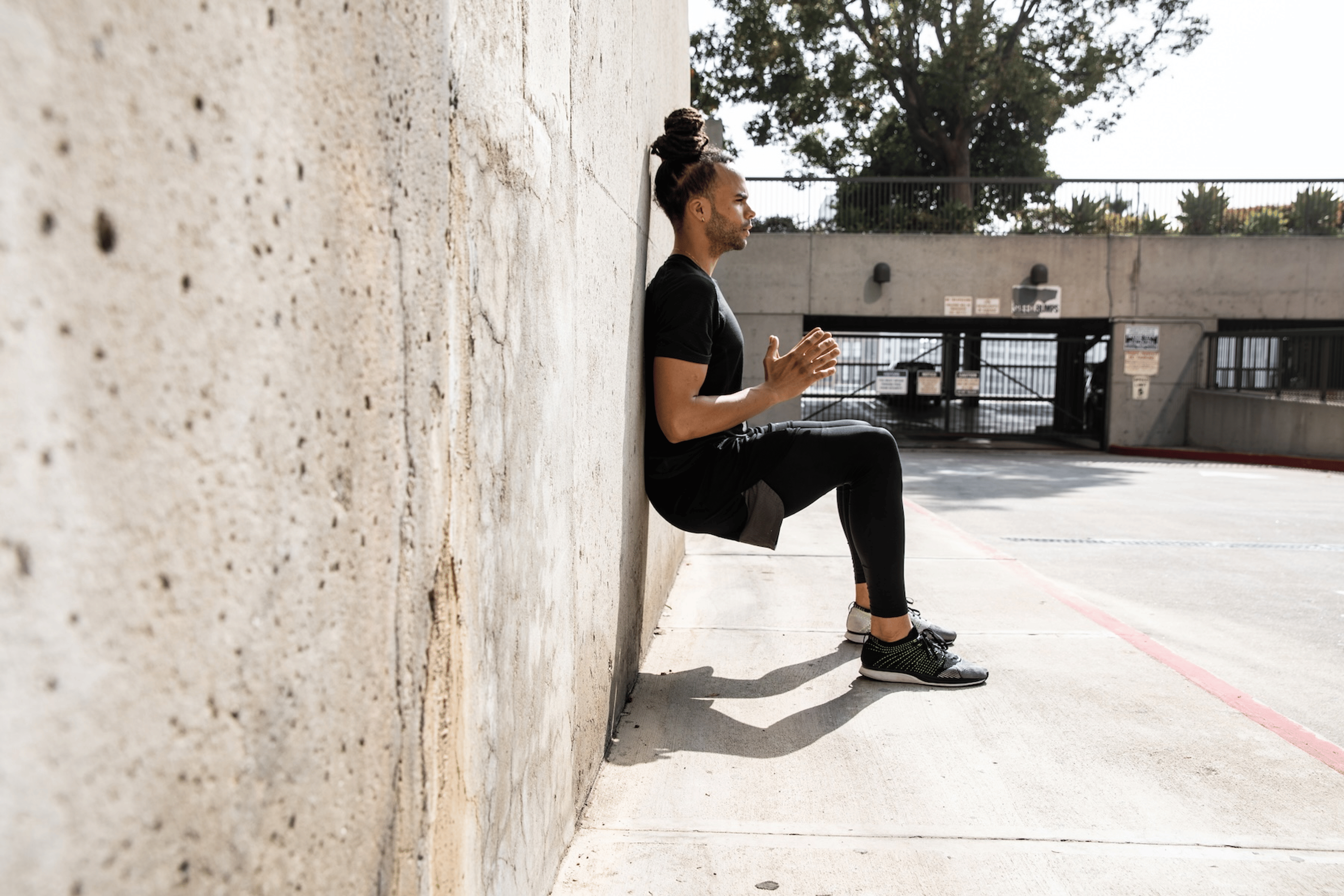 A man holding a wall sit exercise outside.
