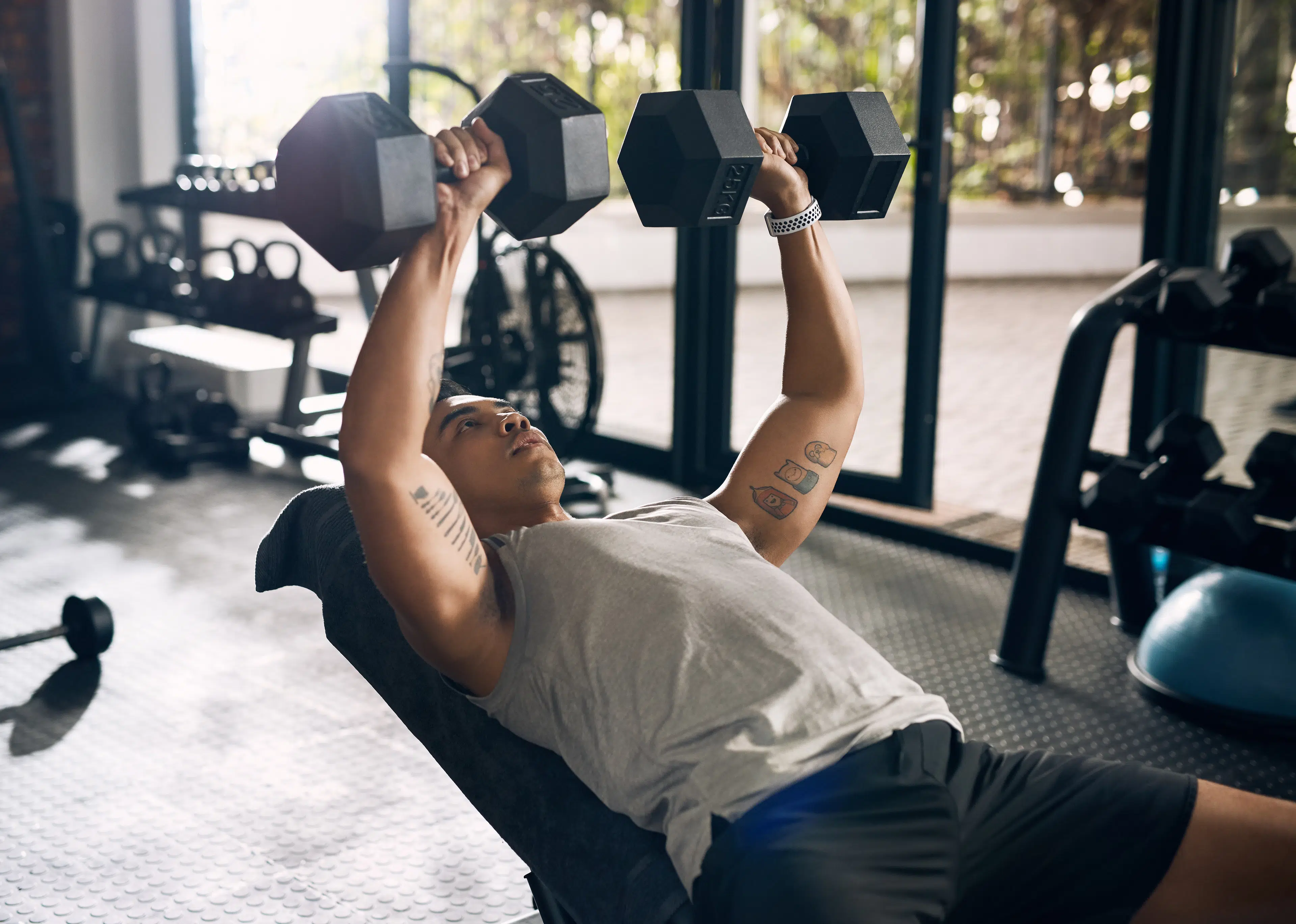 Man performs an incline dumbbell chest press on bench at gym 