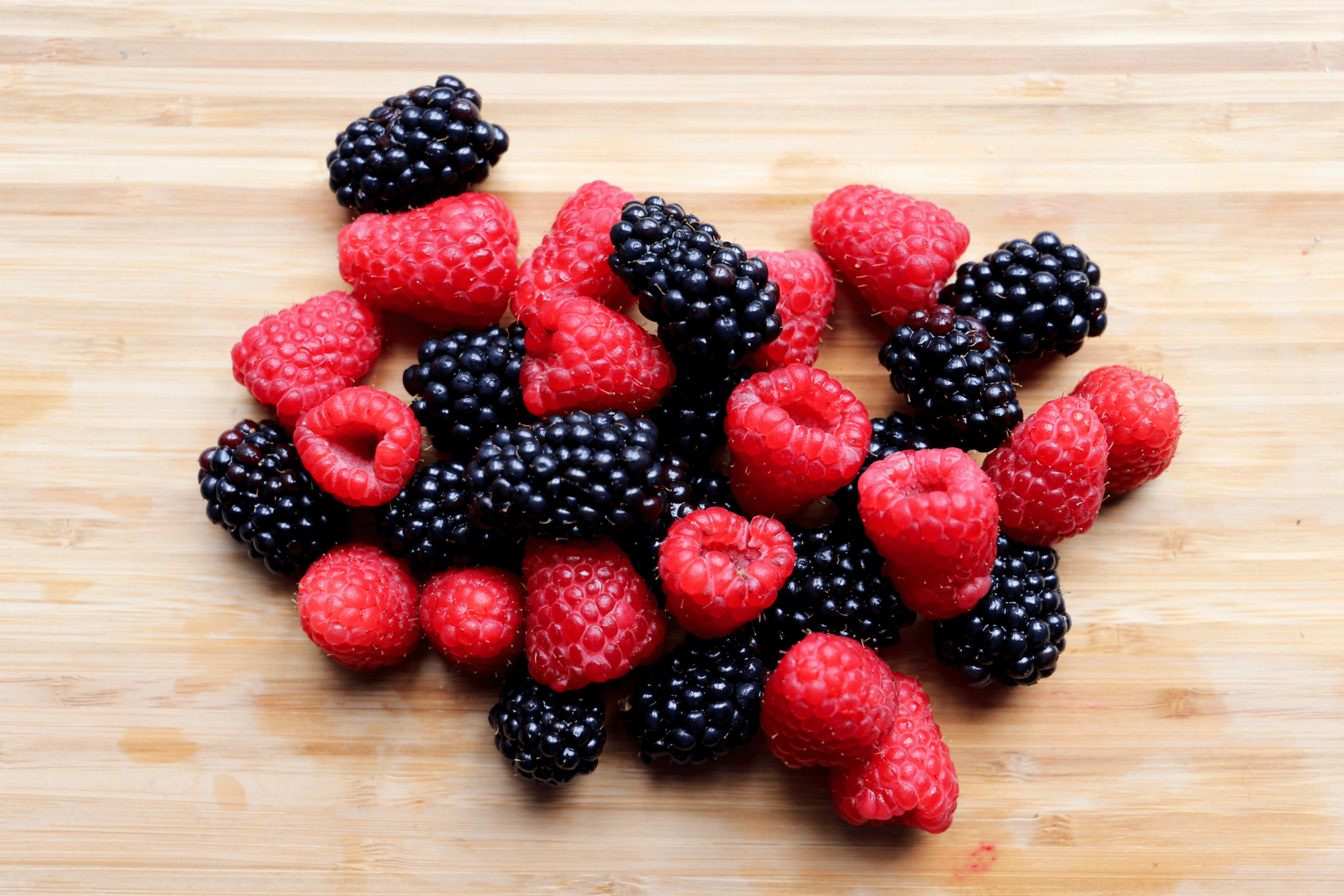 Raspberries and blackberries laying on a flat wooden surface. Berries are a great food for gut health.