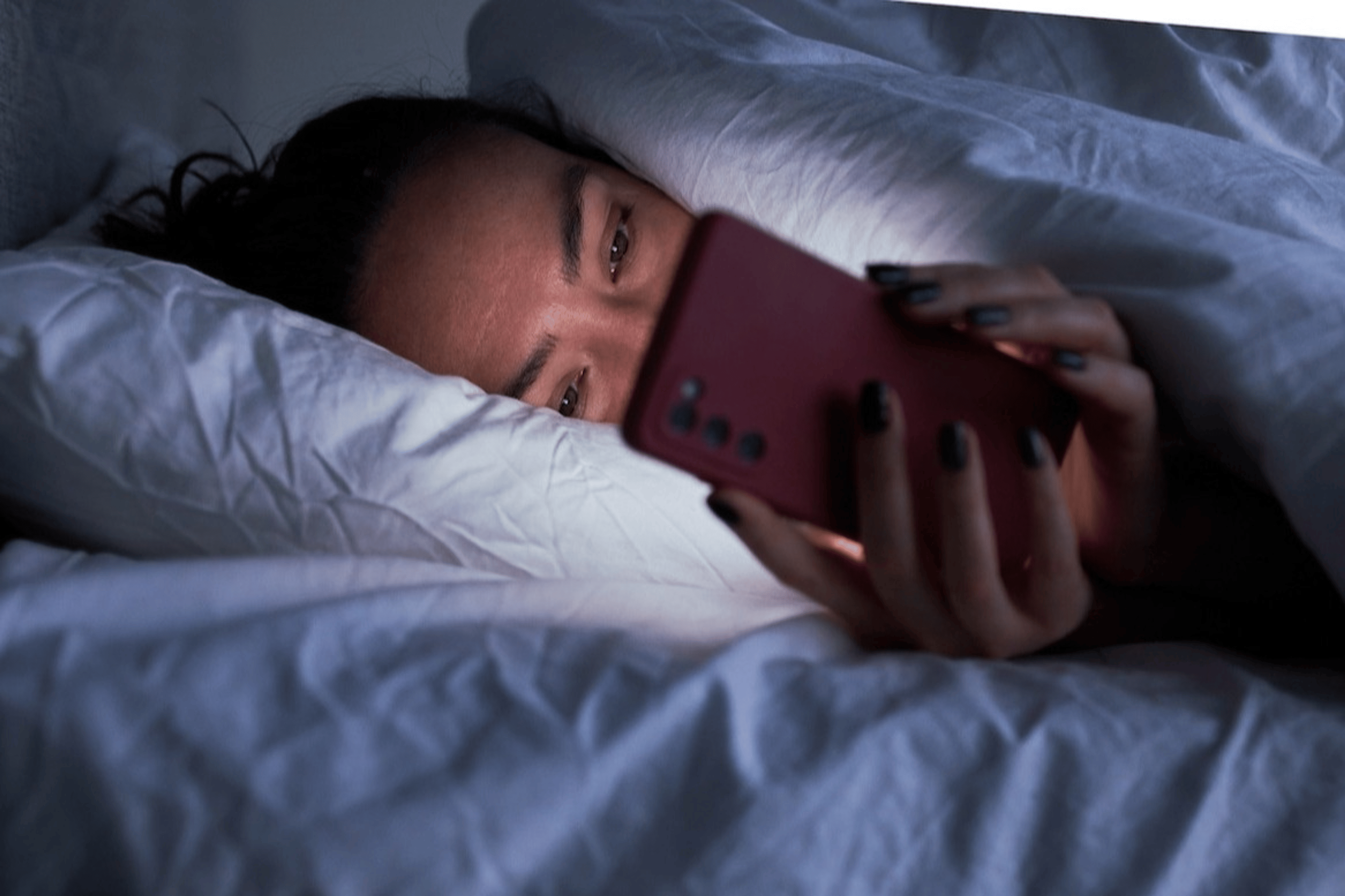 A woman practicing revenge bedtime procrastination by scrolling on her phone in bed late at night.