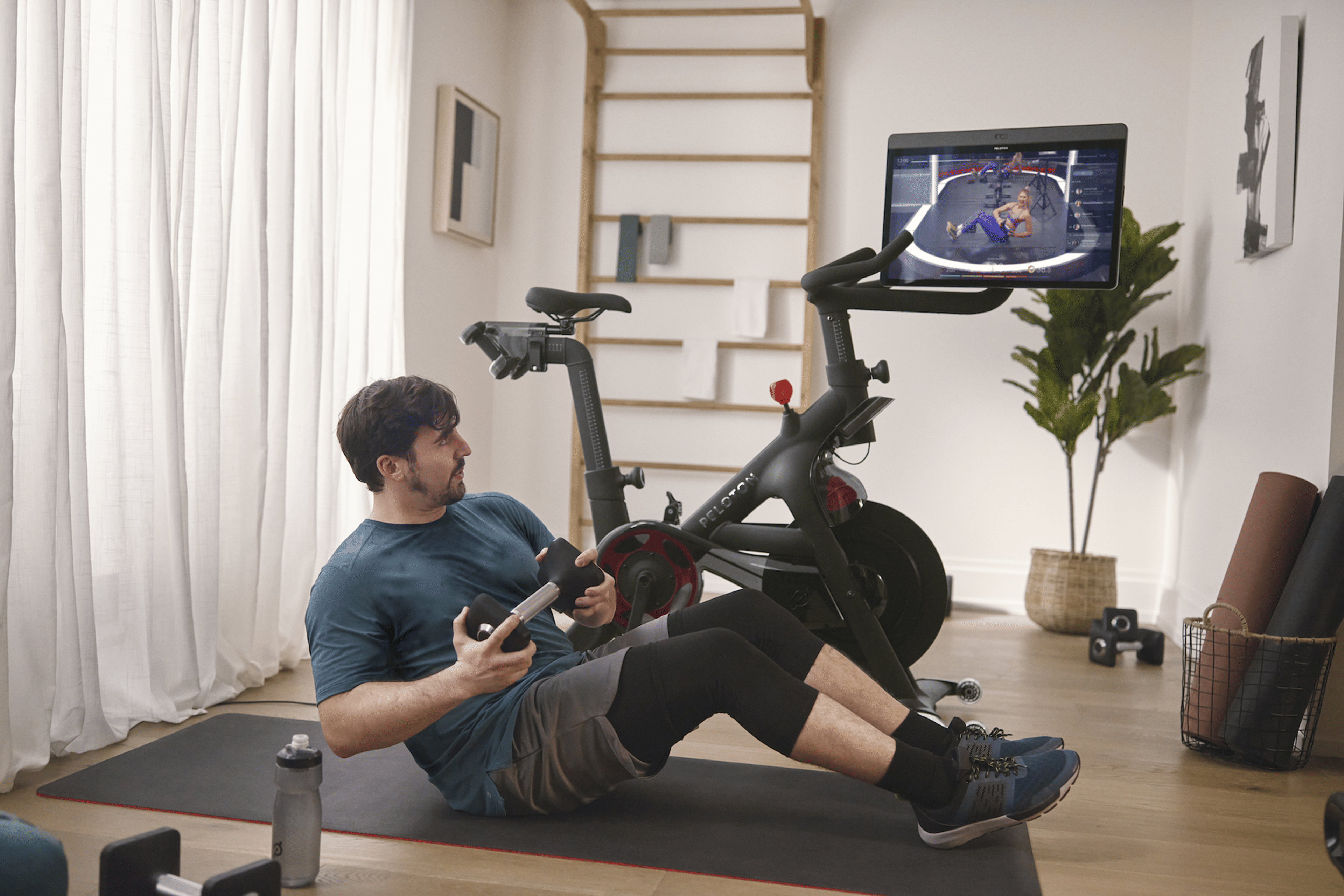 Man does a core exercise on the mat next to Peloton Bike. 