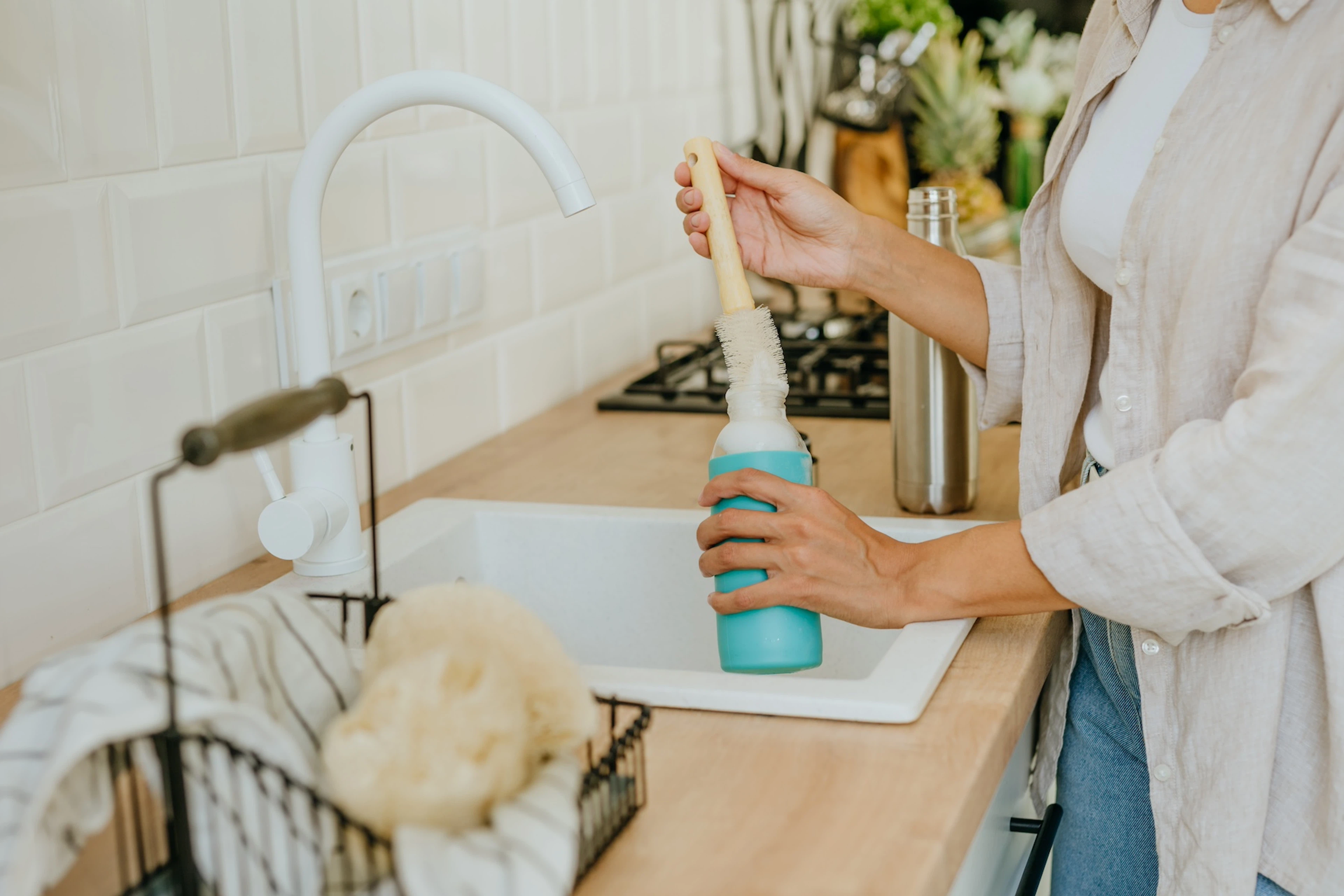 A woman cleaning a water bottle using a brush in the kitchen sink.