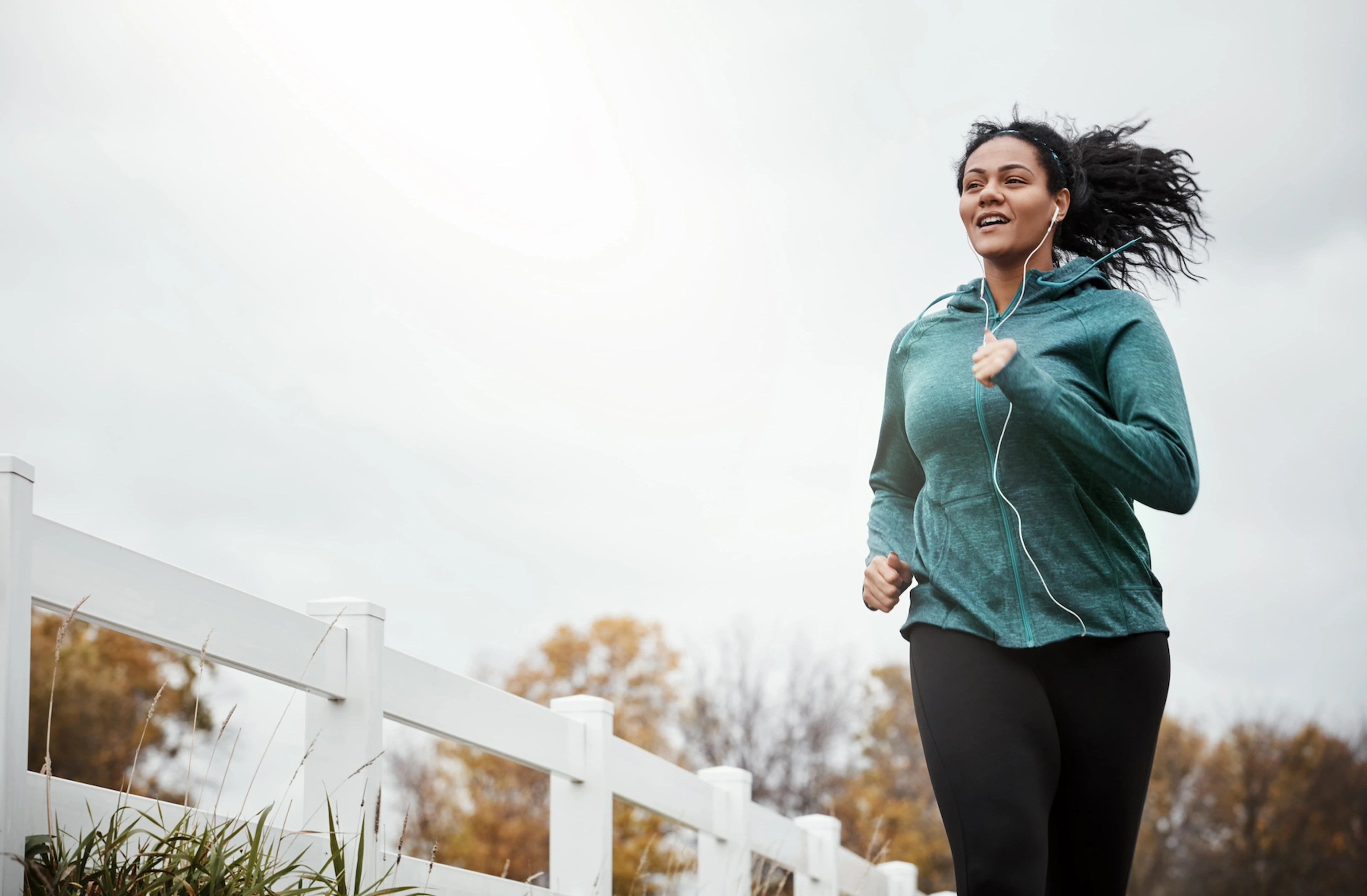 A woman happily running outside while listening to headphones. Read inspirational running quotes in this article.