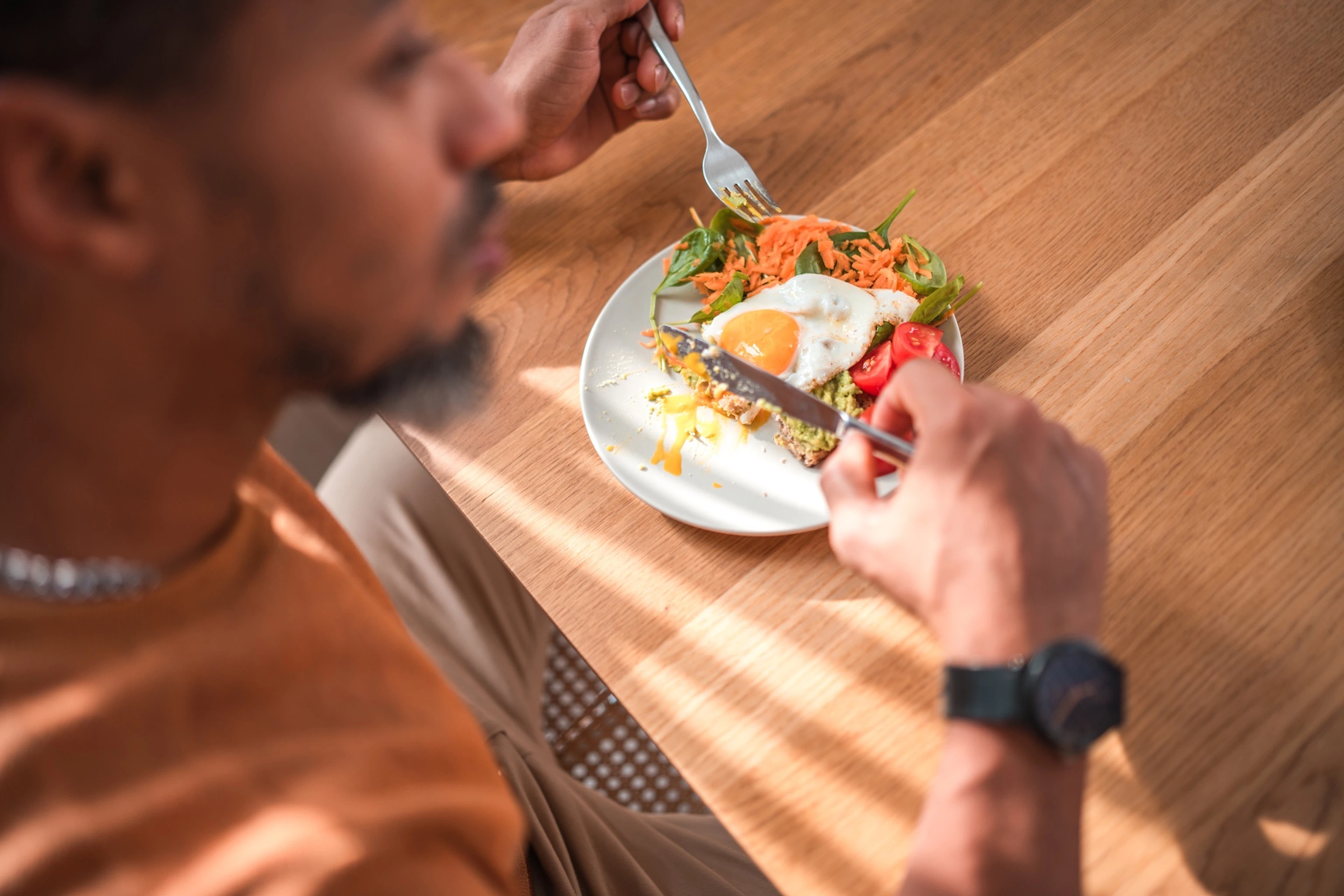 A man eating breakfast for dinner after a workout. His plate has a fried egg with a side salad.