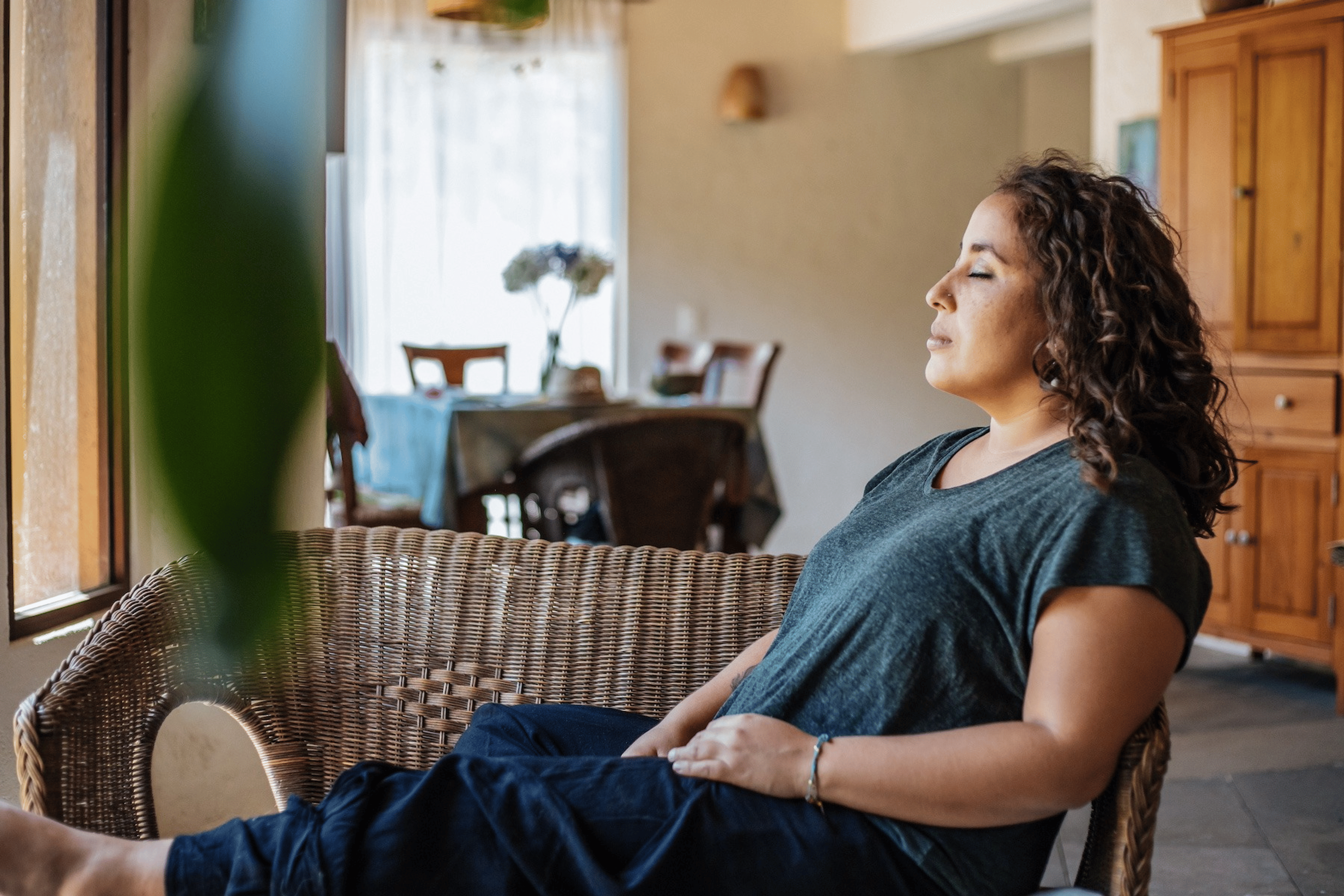 A woman sitting in her home, closing her eyes, and calmly manifesting something.