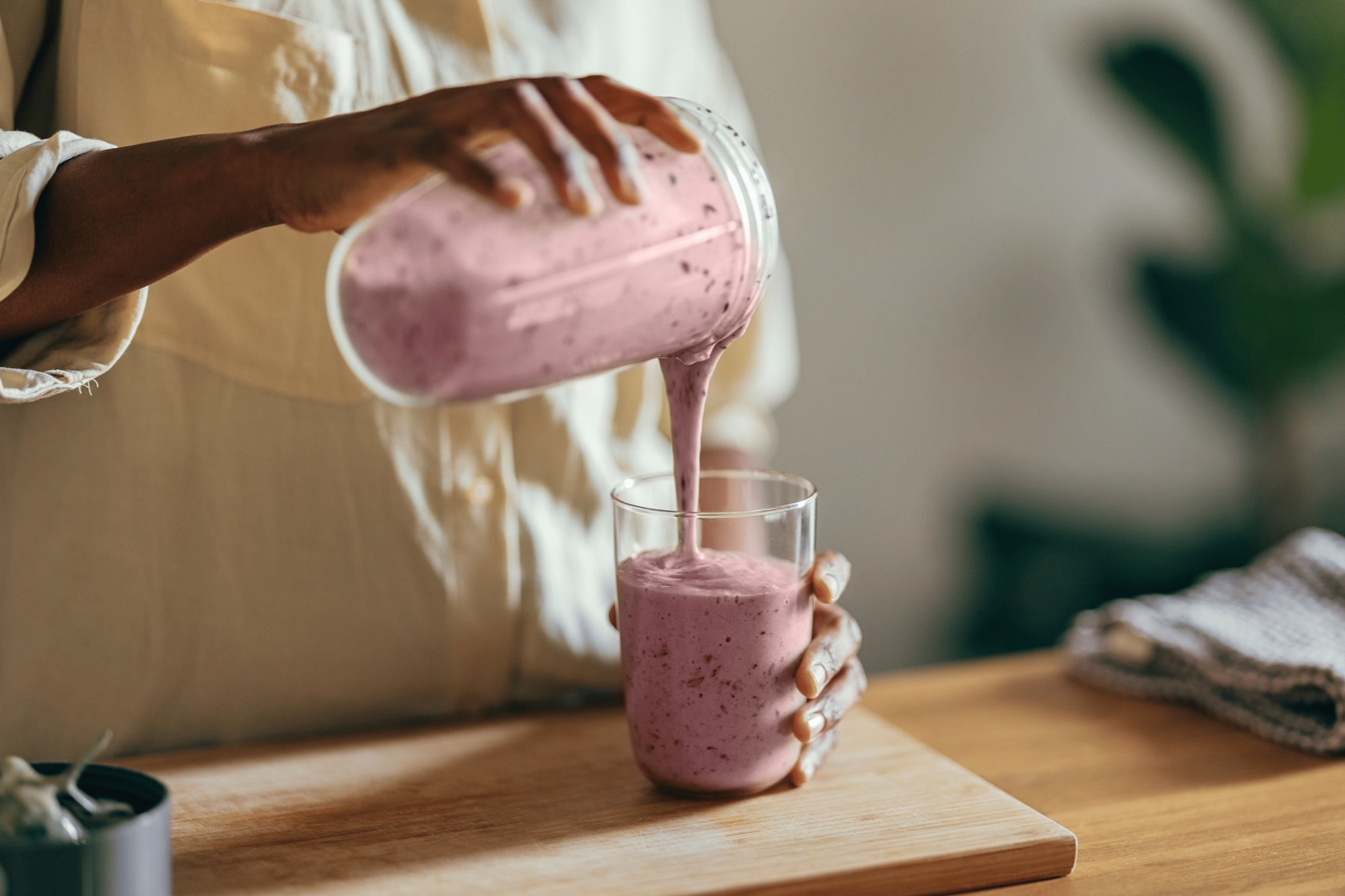 A close-up photo of a person pouring a high-protein smoothie into a glass.