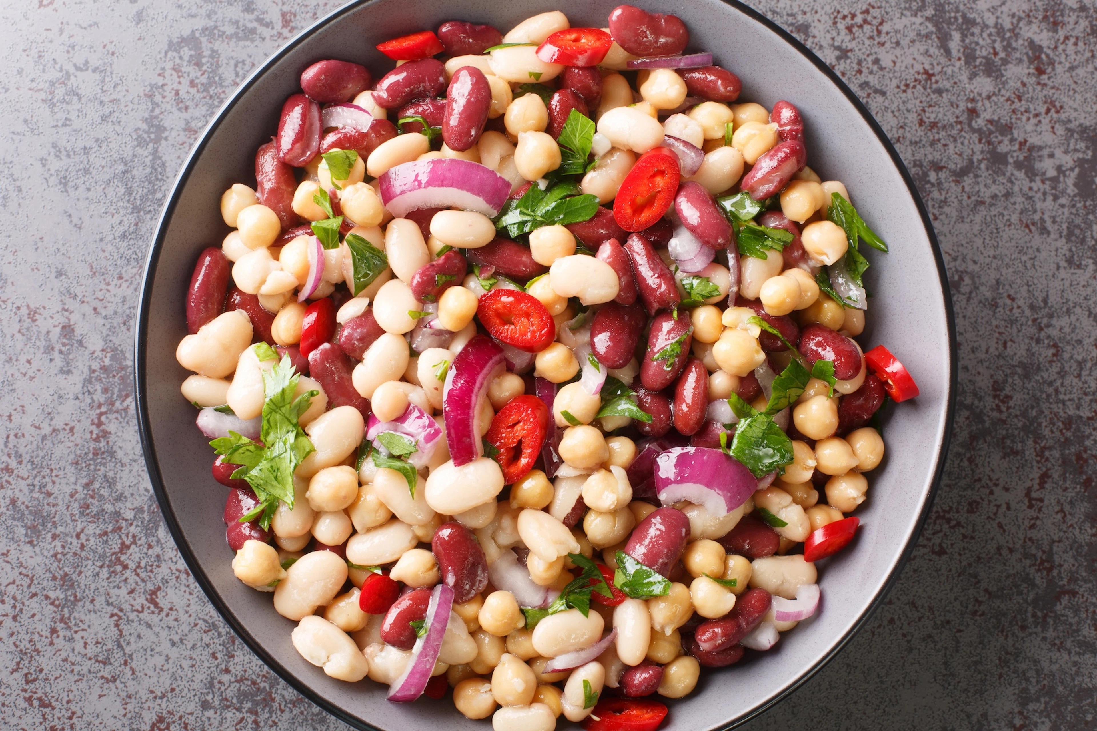 A bowl of three-bean salad featuring cannellini beans, garbanzo beans, and kidney beans, among other ingredients.